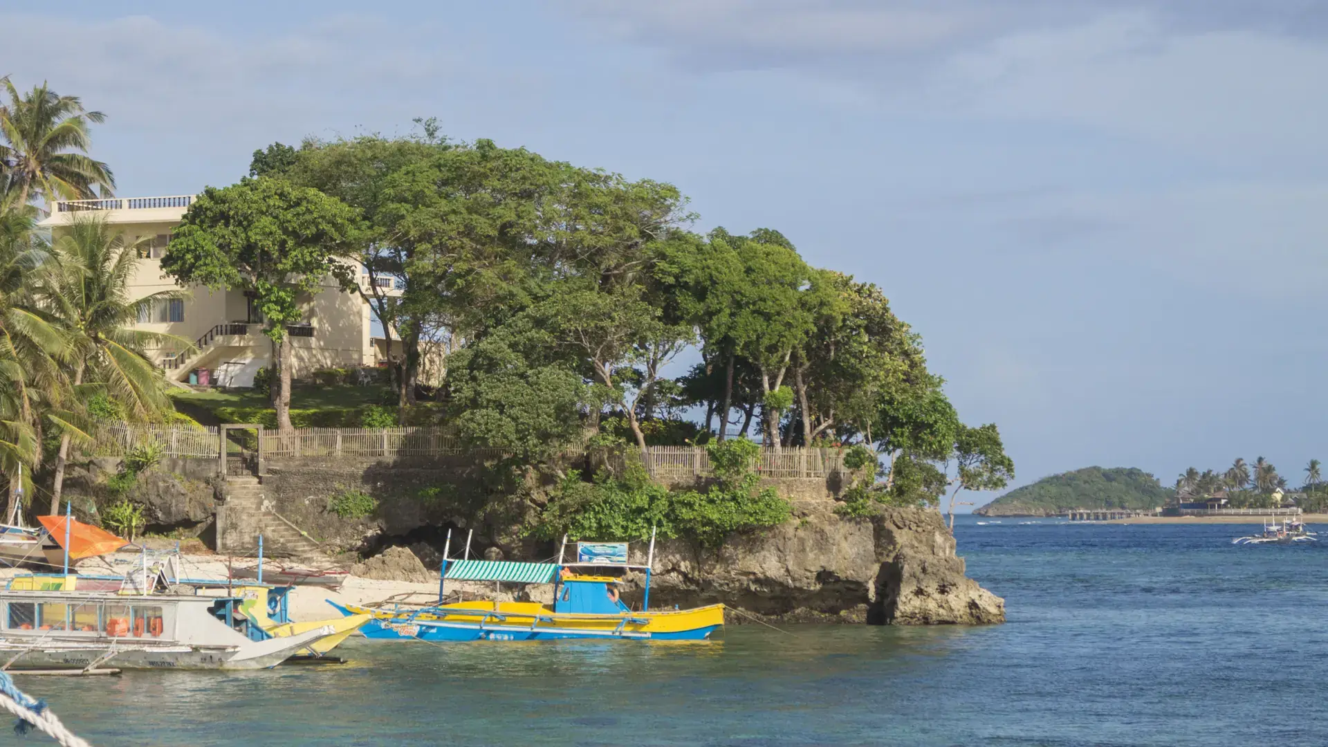 Rocky headland with a building, trees and moored outrigger boats on Boracay’s southern coast