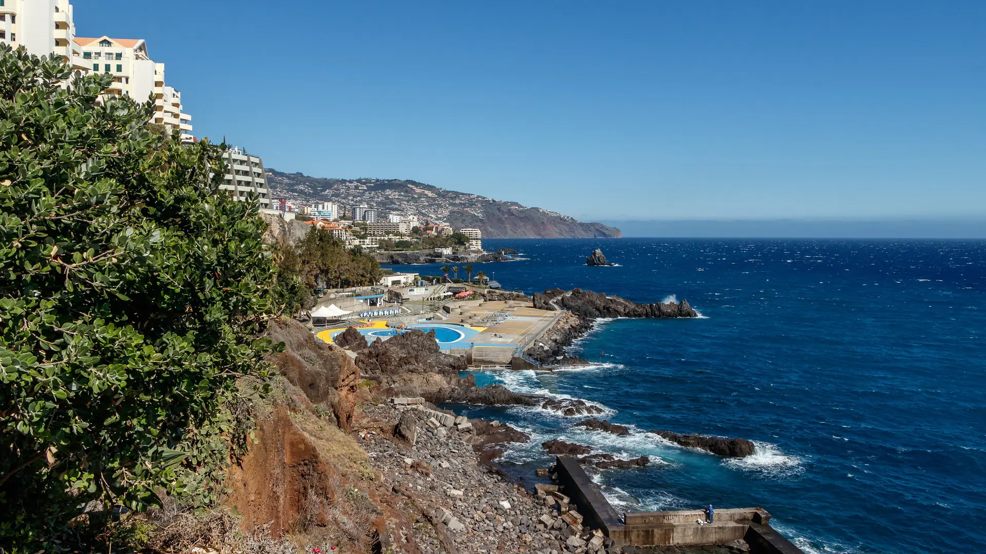 Swimming pools and rocky Atlantic shore along Funchal’s Lido seafront under a clear blue sky
