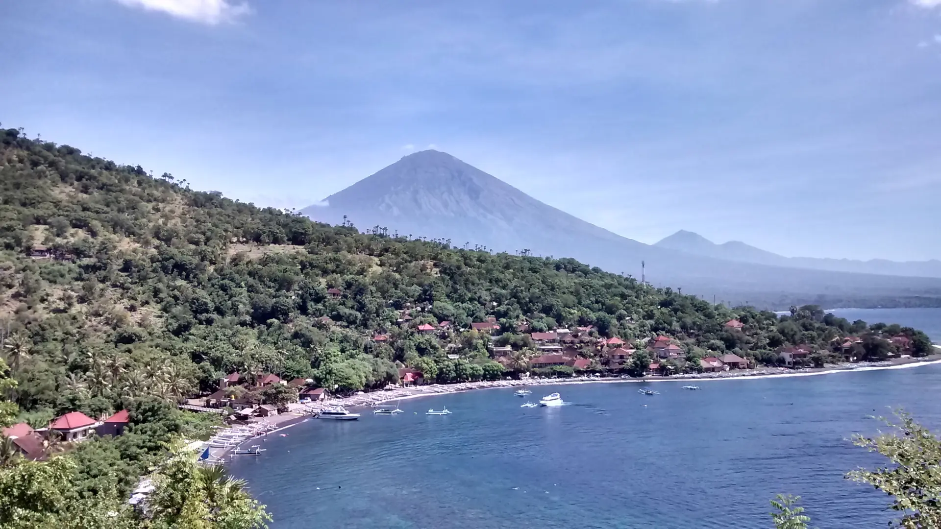 Jemeluk Bay’s curved shoreline and boats beneath Mount Agung on Bali’s Amed coast