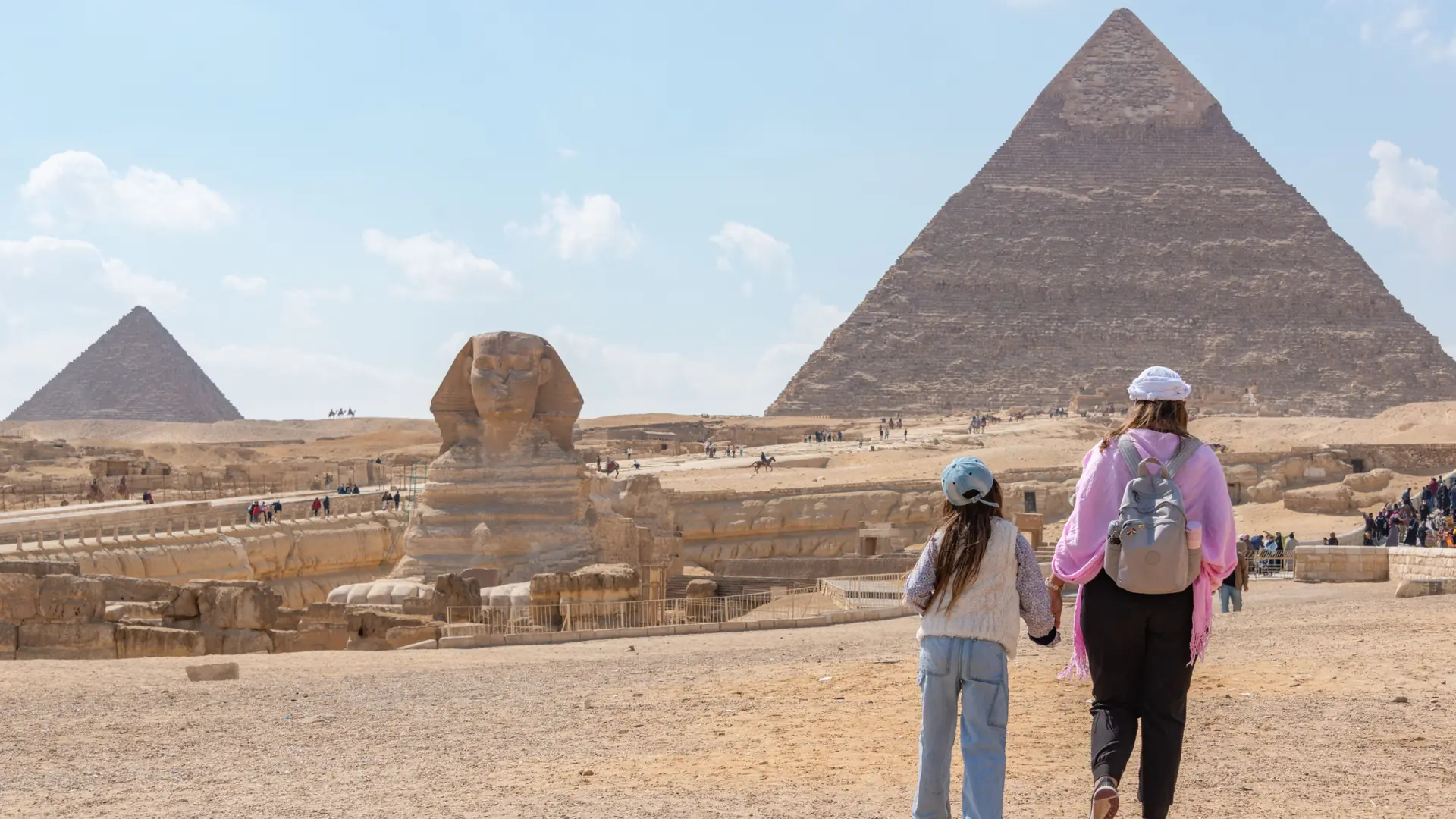 Visitors approaching the Great Sphinx with Giza pyramids in sunshine