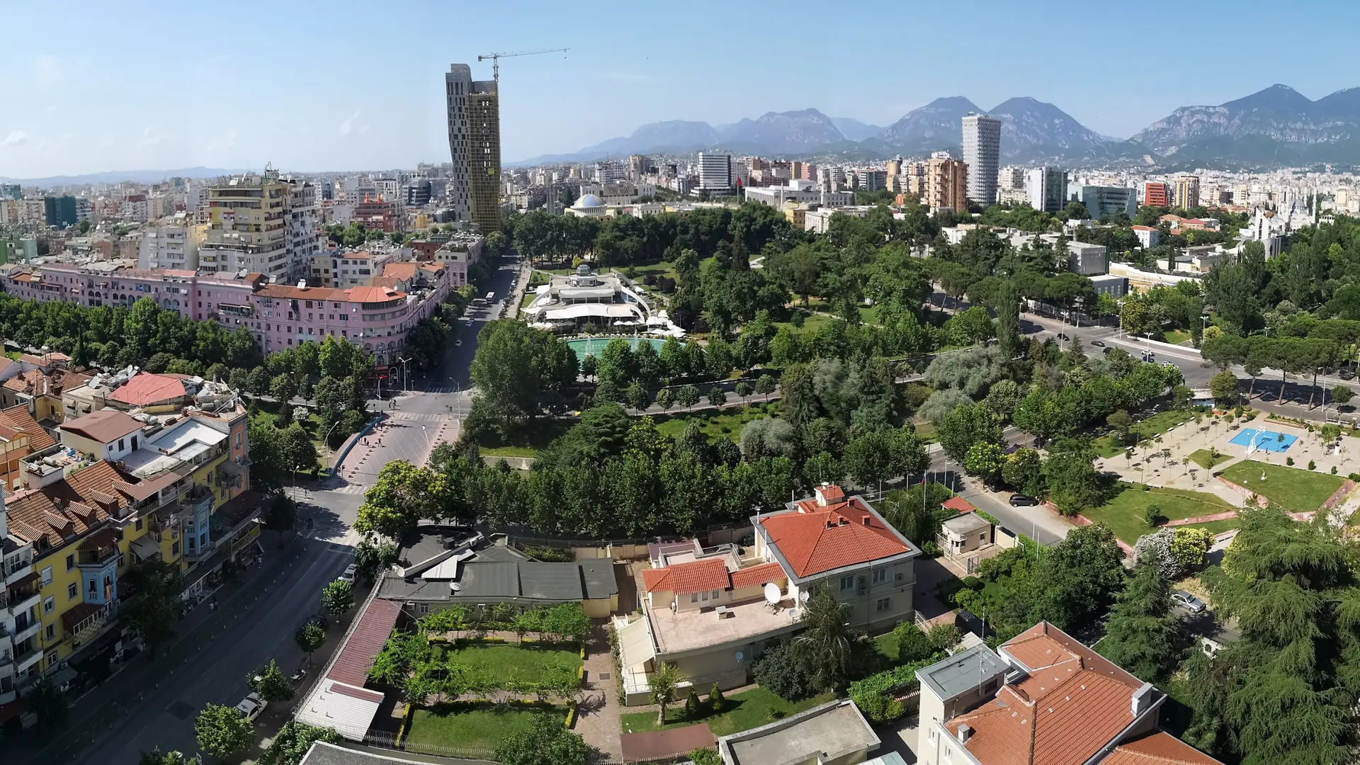 Central Tirana's towers and green parks below the mountains on a sunny day