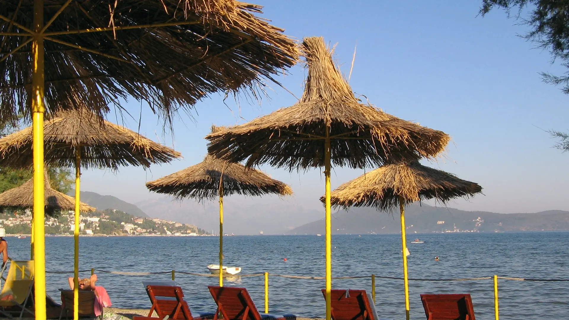 Straw beach parasols on Igalo's shoreline beside the Bay of Kotor