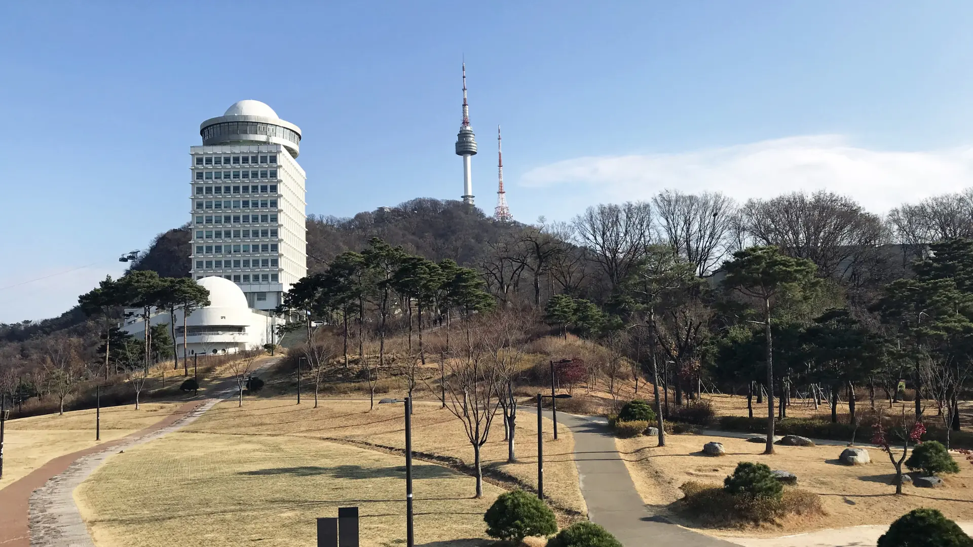 N Seoul Tower atop the forested Namsan hill under a clear blue sky, with the city spread out below