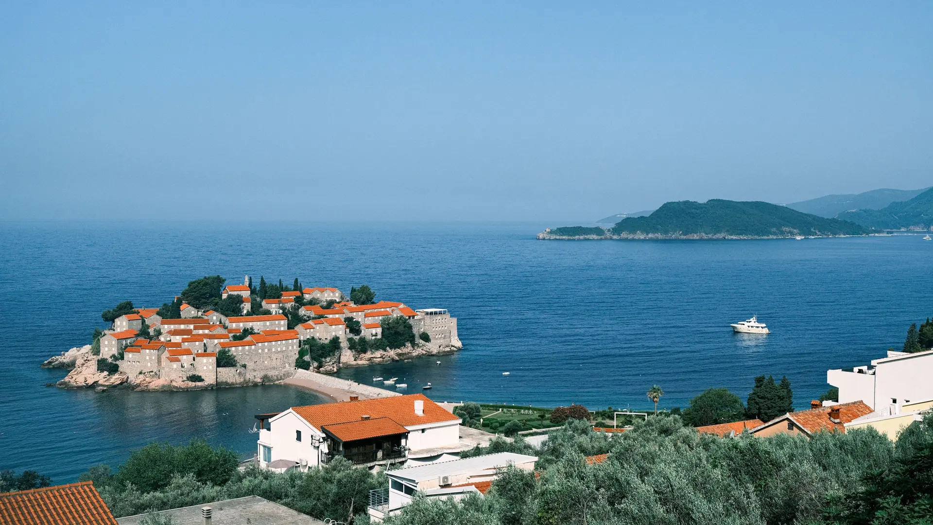 Sveti Stefan island and Adriatic Sea seen above mainland village rooftops