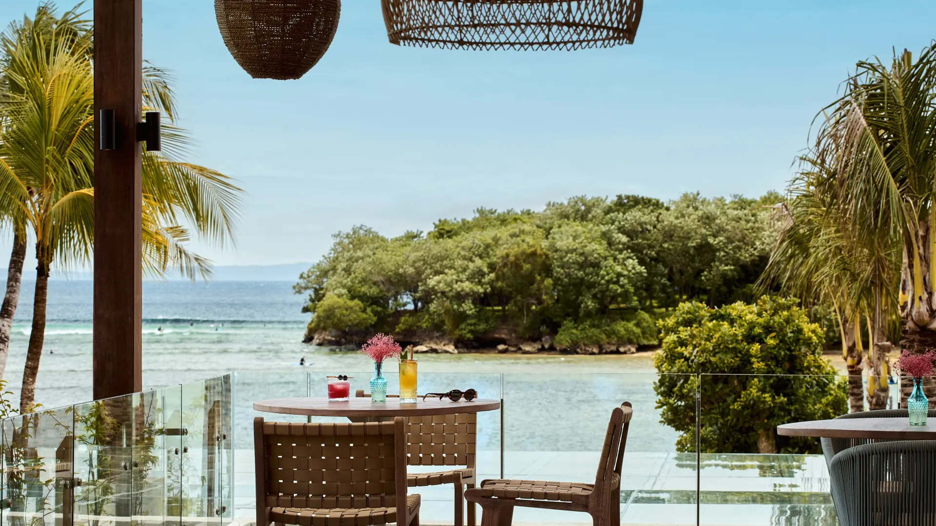 Outdoor tables, palms and an ocean view at Kanna Rooftop in Paradisus Bali, Nusa Dua