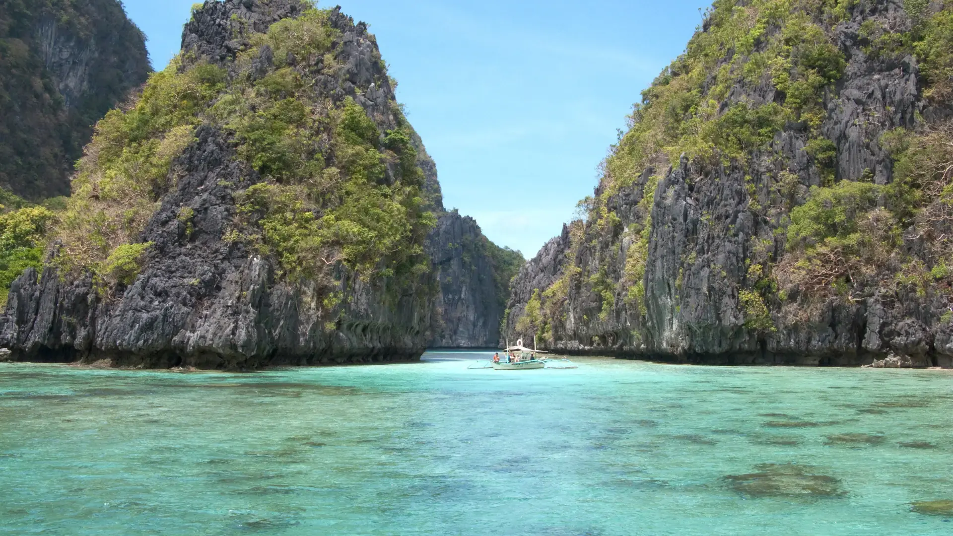 Sunlit limestone cliffs and a bangka on turquoise water in Bacuit Bay, El Nido