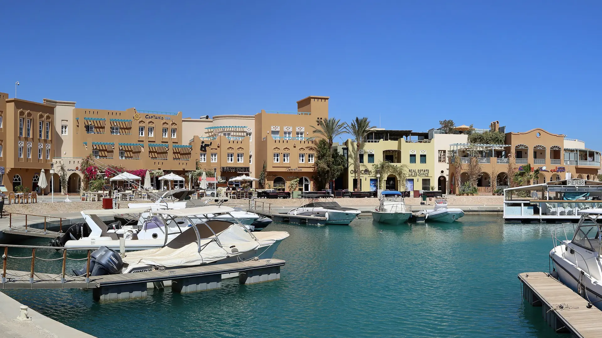 Sunny Abu Tig Marina in El Gouna with moored yachts, waterside buildings and blue lagoon water.