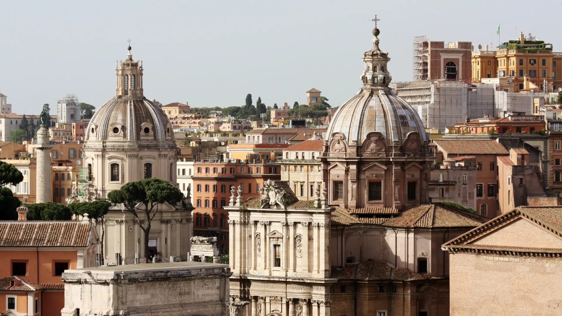 A sunlit wide view over Rome rooftops, domes and terracotta buildings