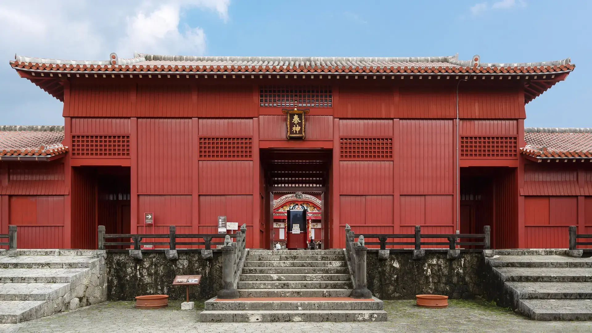 Shureimon gate glowing red against blue sky in green Shurijo Castle Park