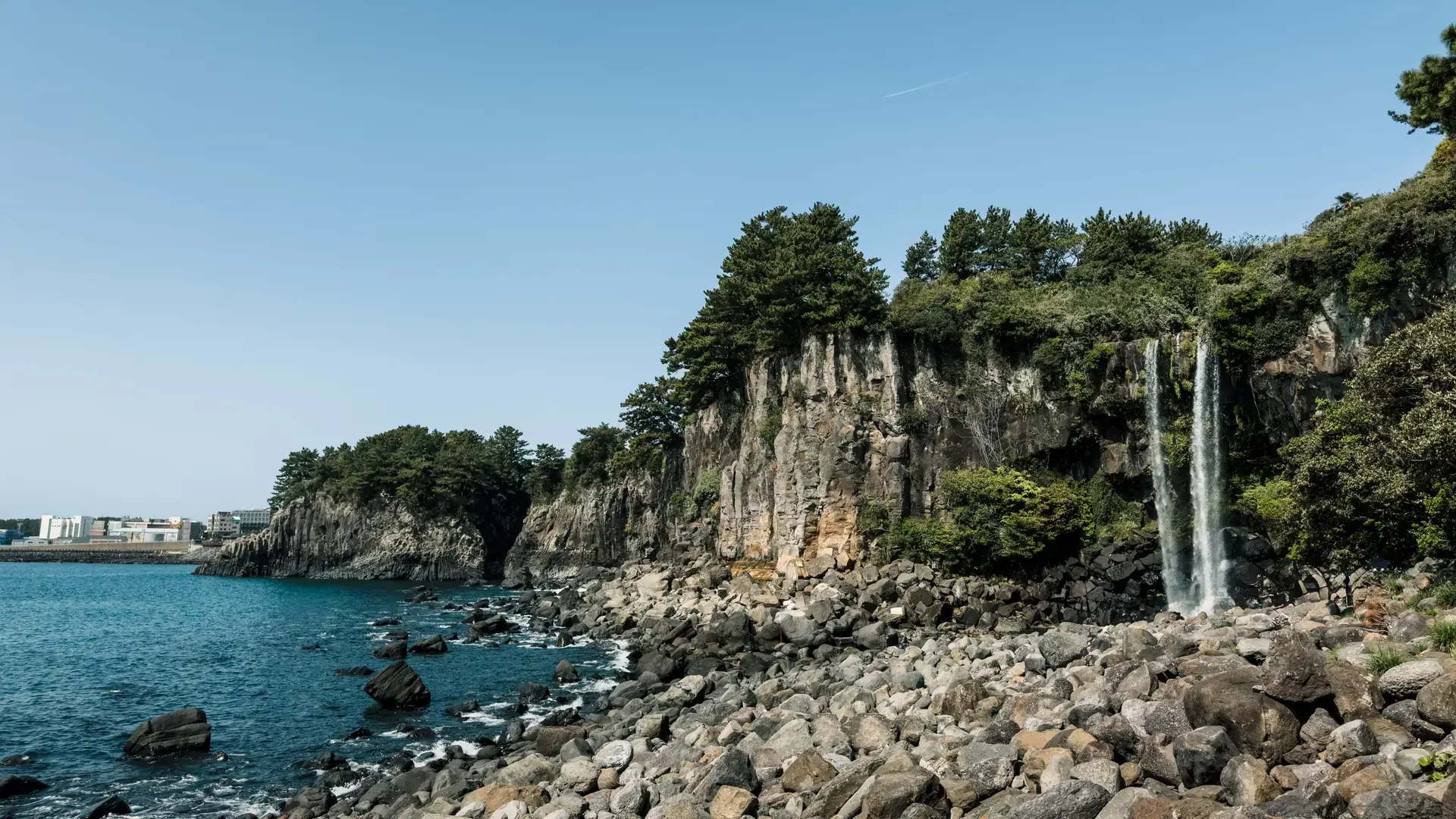 Jeongbang Waterfall drops from a wooded cliff onto the rocky shore at Seogwipo