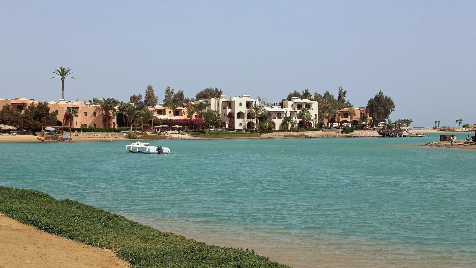 Sunny El Gouna lagoon with low waterfront buildings, palms and turquoise water.