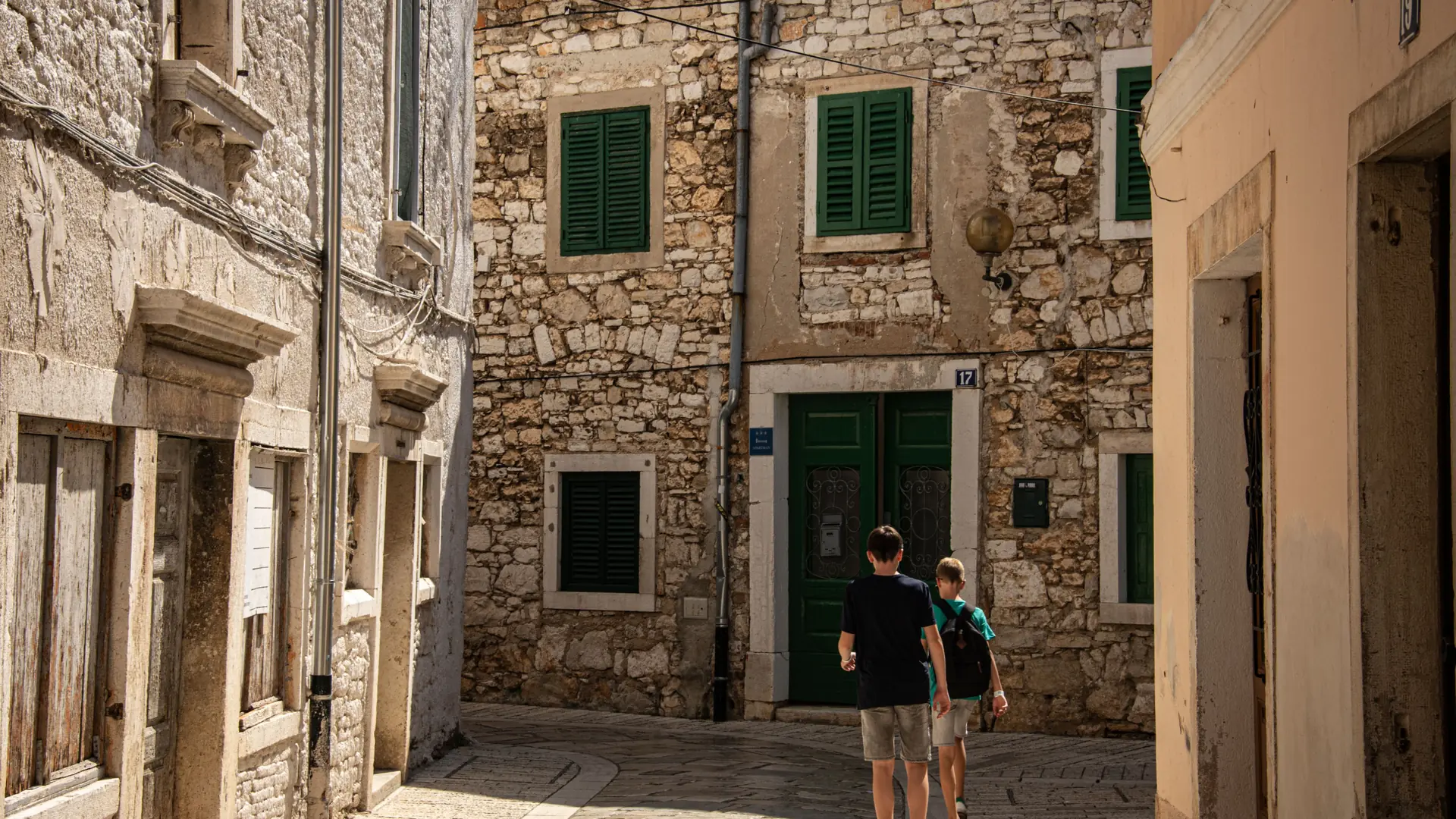 A sunlit stone lane between old houses with green shutters in Split's Veli Varoš