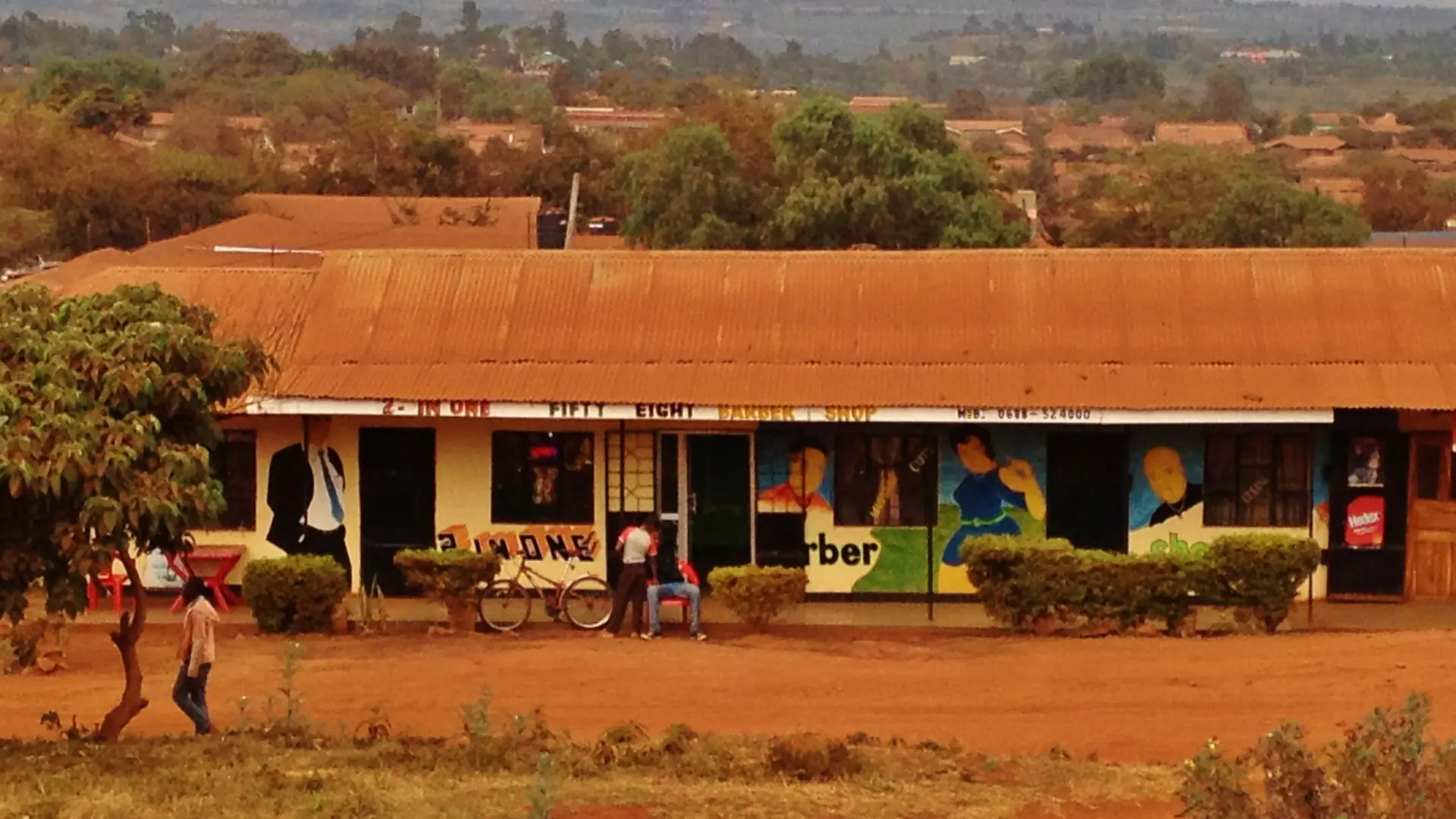 Karatu roadside building with red earth and a distant hillside