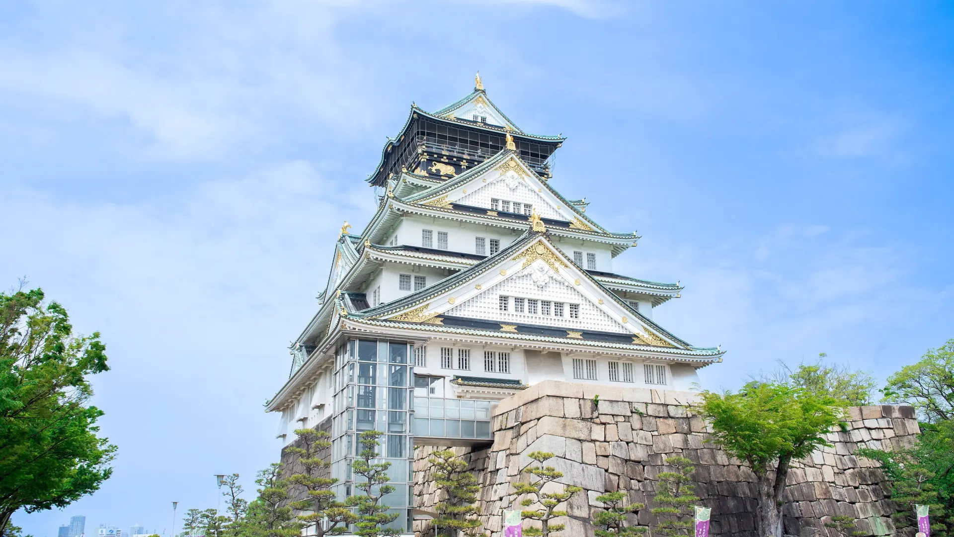 Osaka Castle’s white main keep, stone walls and green trees beneath a bright blue sky