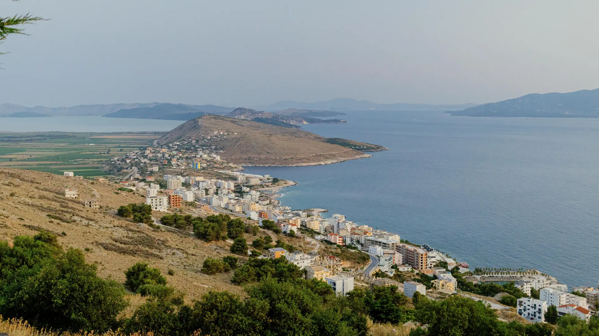 Sarandë's hotels stretching along the coast towards a green headland, seen from the hills above town