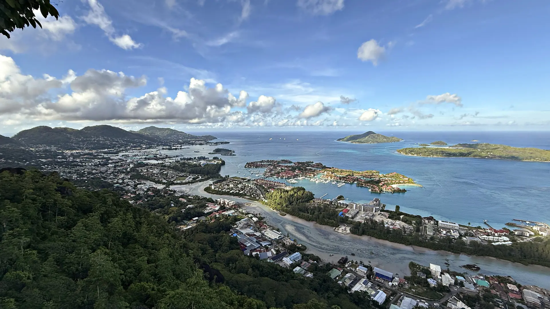 Sunlit panorama of Port Victoria, the Mahé coast and green hills beneath a blue sky