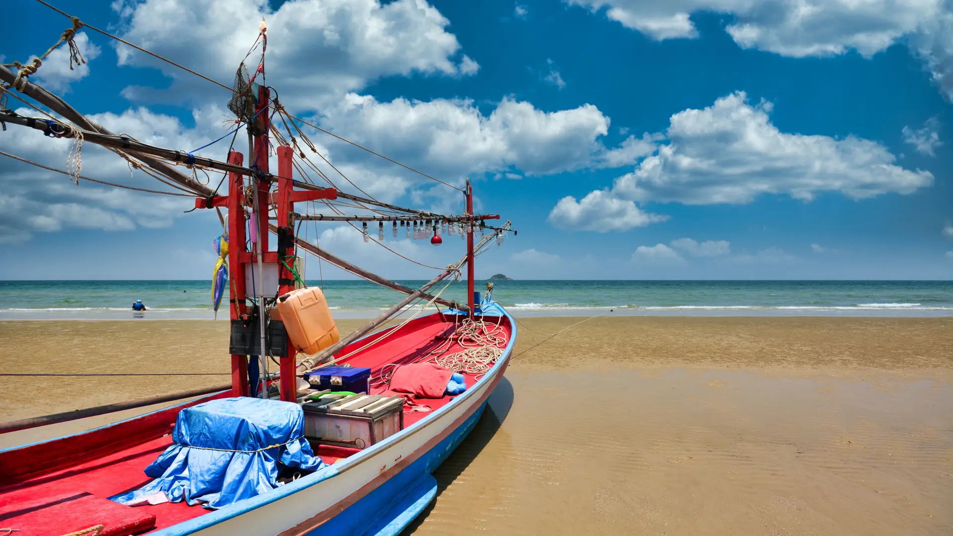 Colourful fishing boat resting on Hua Hin's sand beneath a clear blue sky