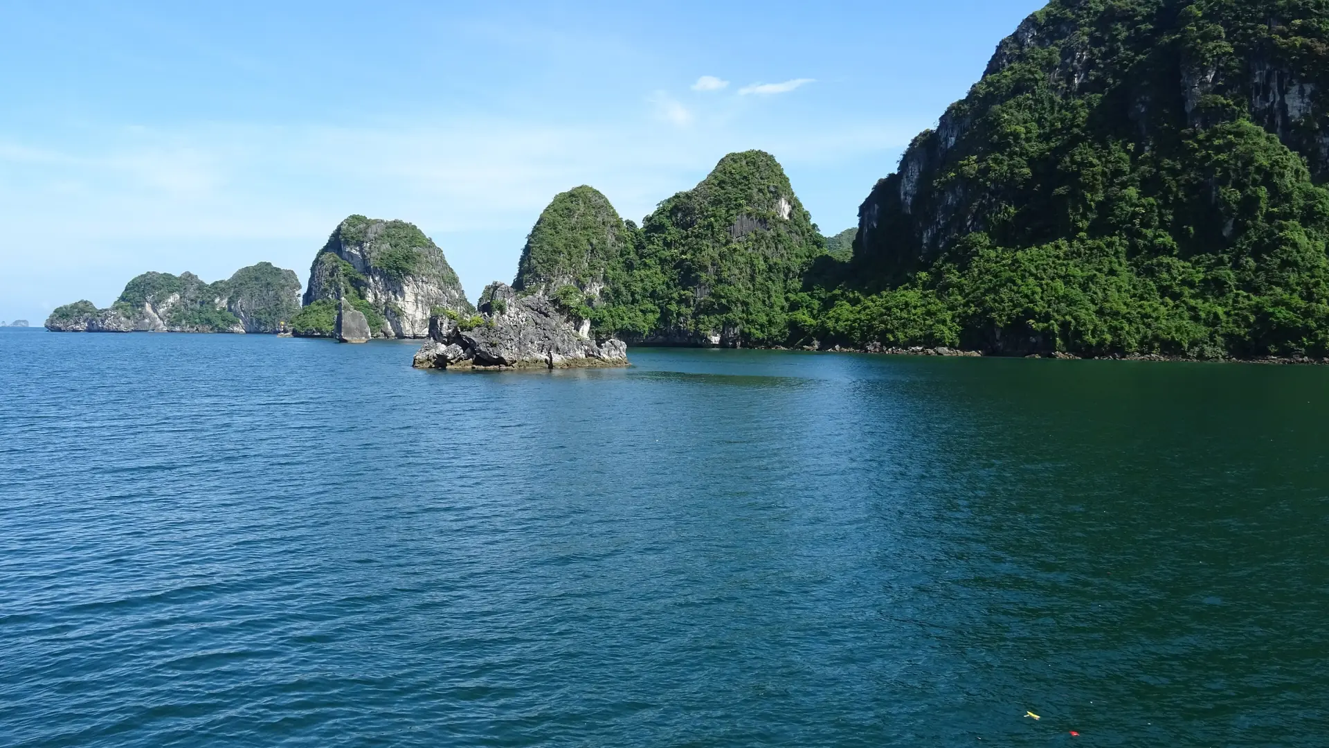 Sunlit limestone islands rising from blue-green water in Ha Long Bay beneath a blue sky