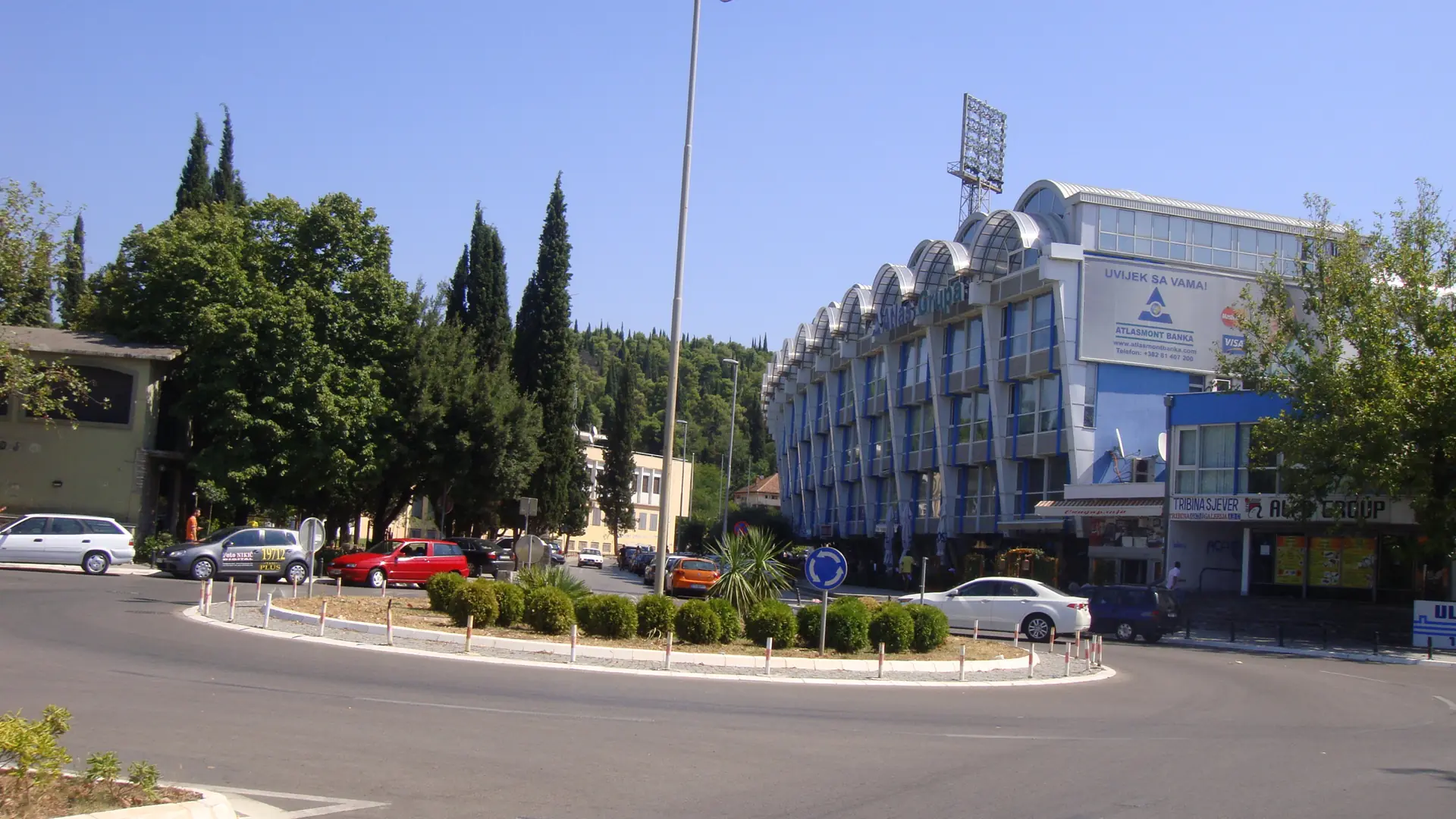 A tree-lined central Podgorica road beside blue-gray city buildings