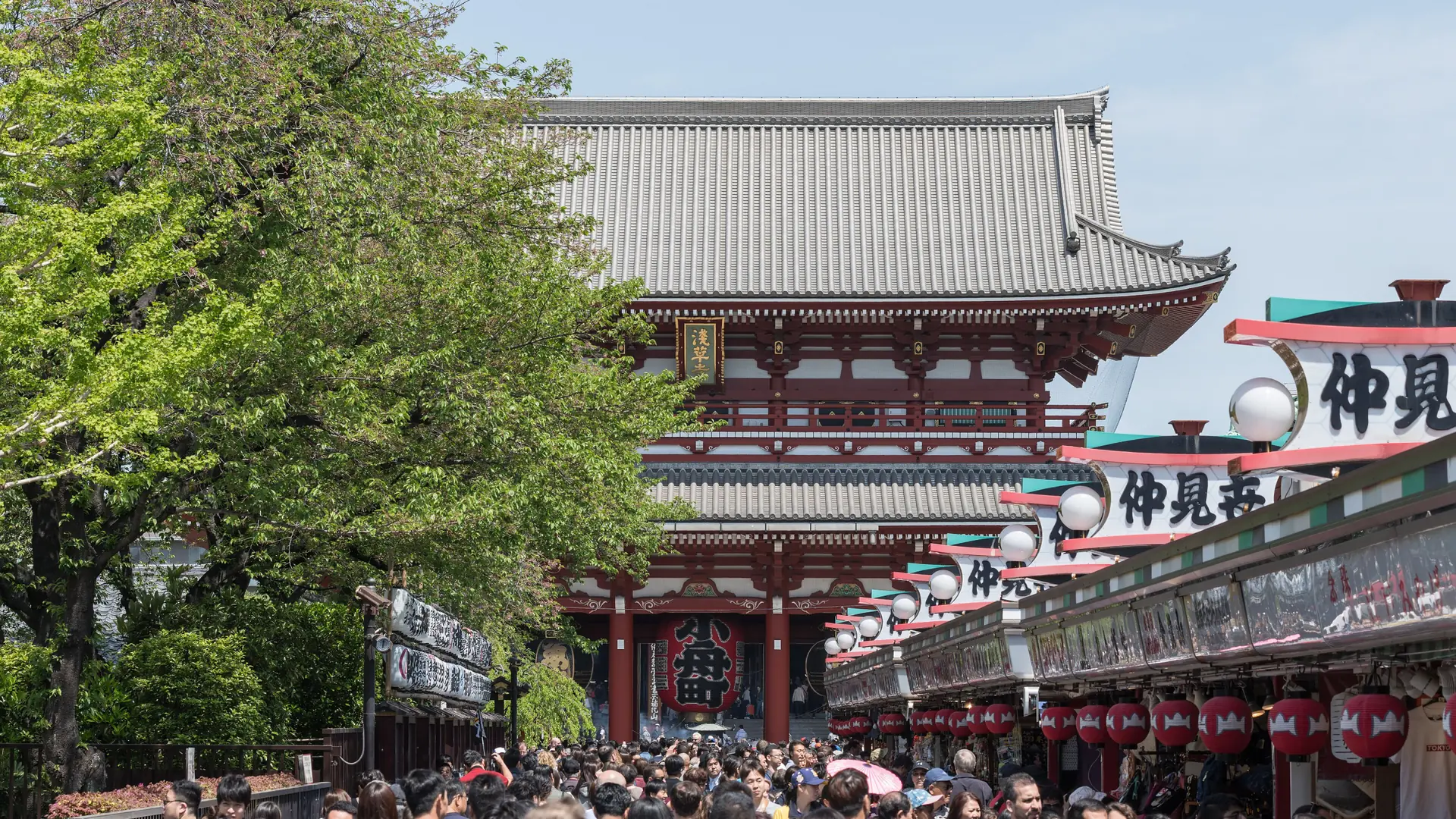 Hozomon Gate above Nakamise’s shop roofs and pedestrians in sunny Asakusa, Tokyo.