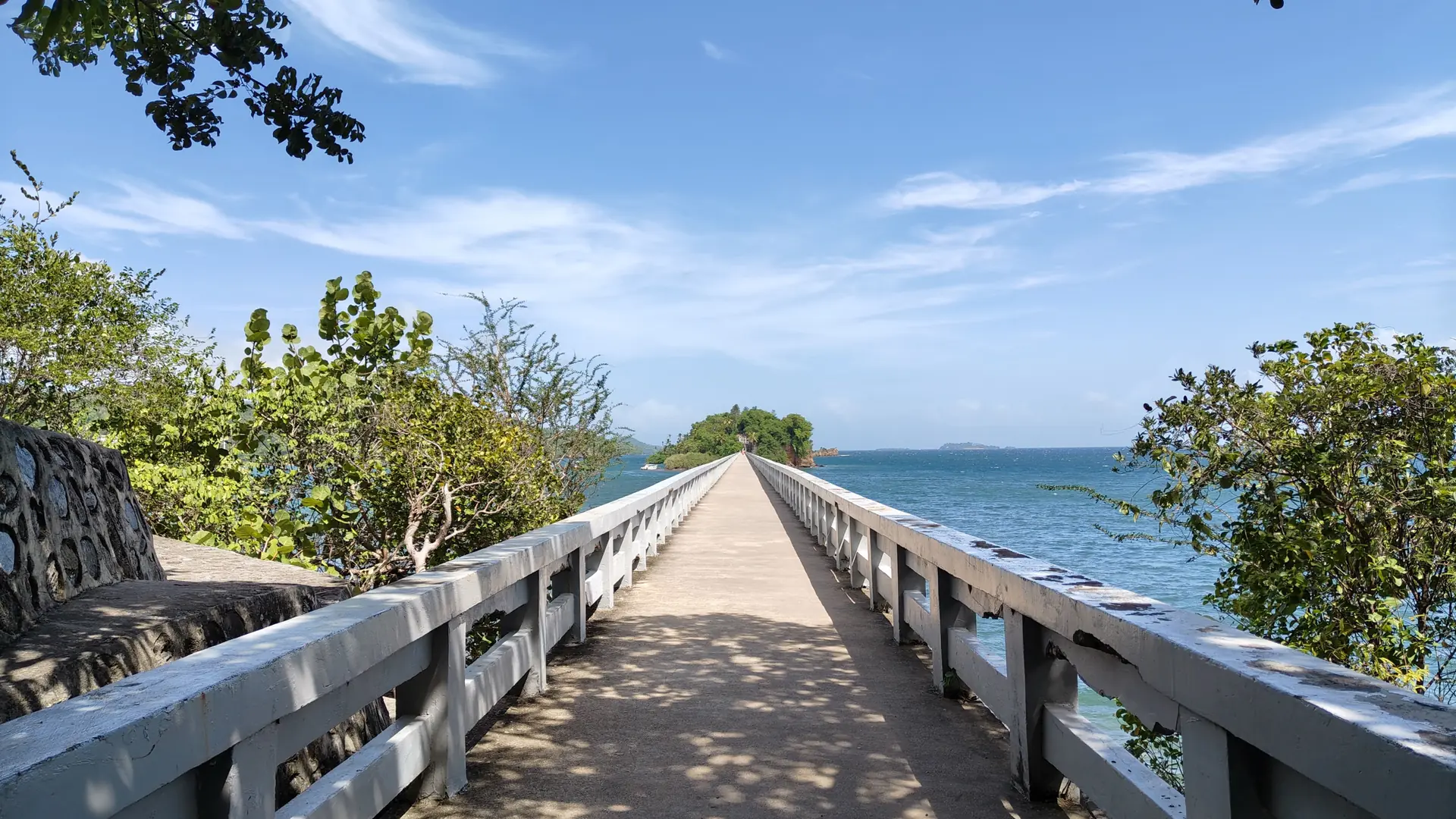 Sunny concrete footbridge leading toward a green islet beside Santa Bárbara de Samaná