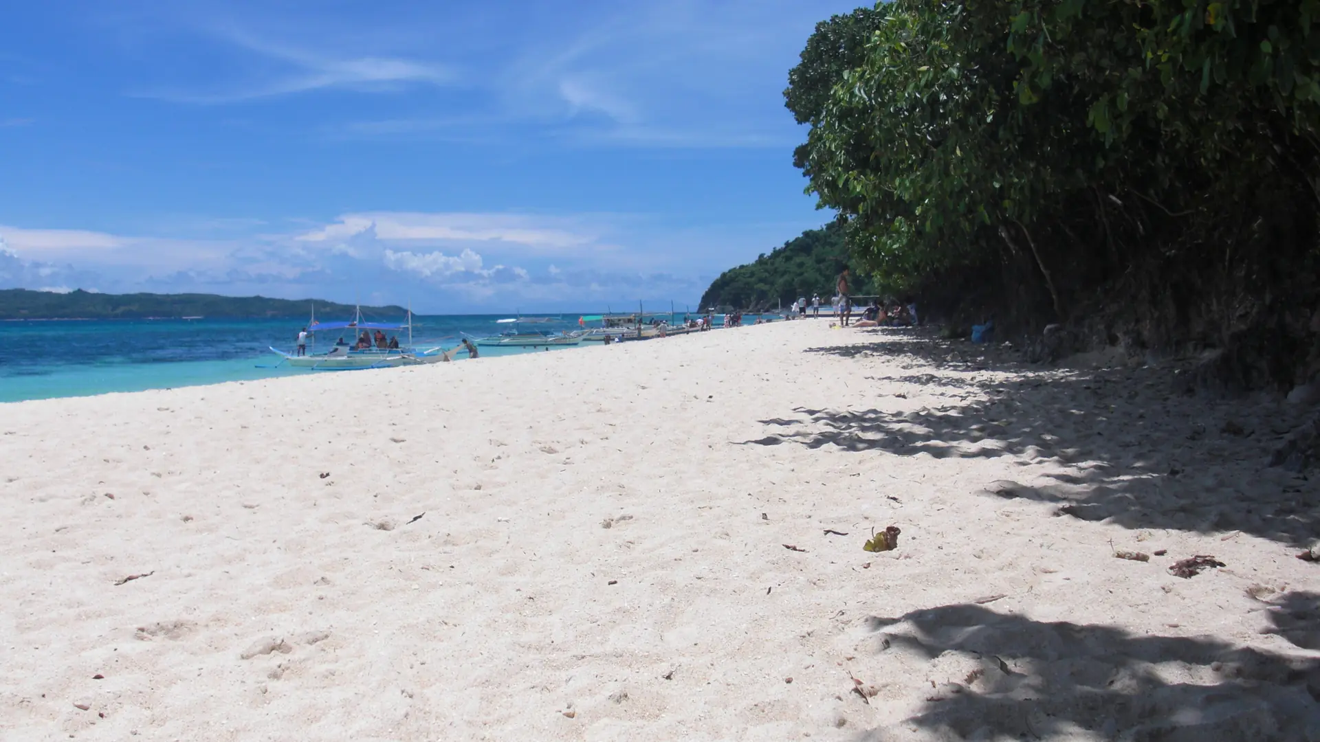 Sunlit sand, trees and outrigger boats at Yapak Beach on Boracay’s northern coast