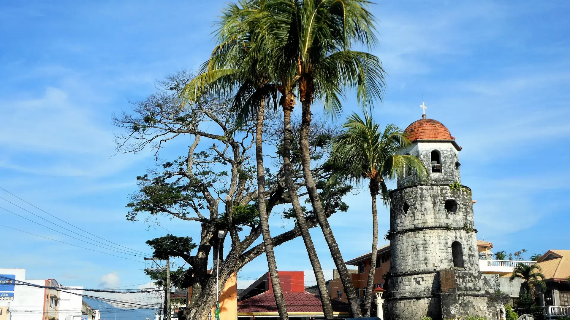 Dumaguete’s stone belfry among palm trees beneath a blue sky