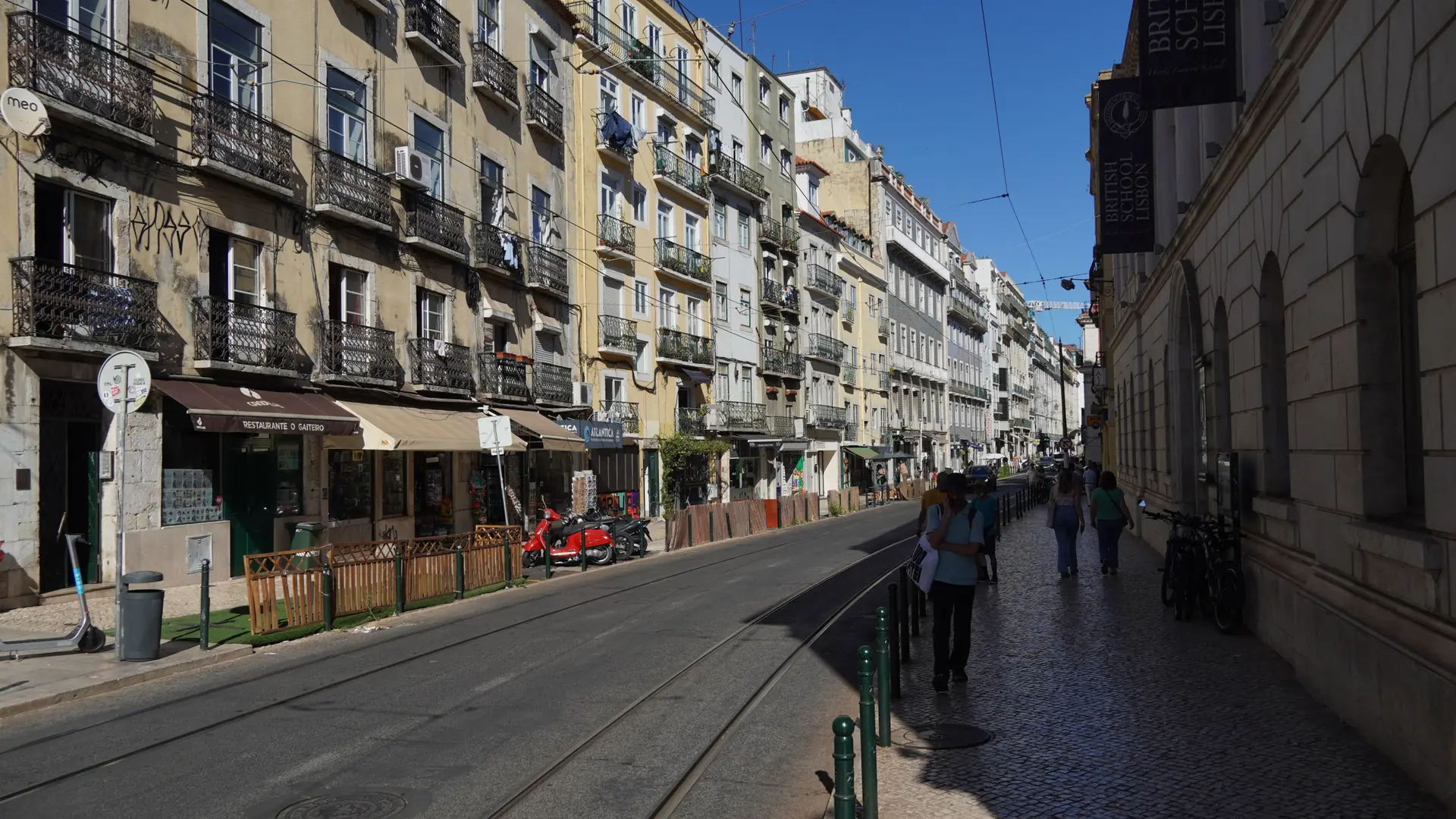 a sunlit Lisbon street near Chiado with tram tracks and cream façades under a clear blue sky