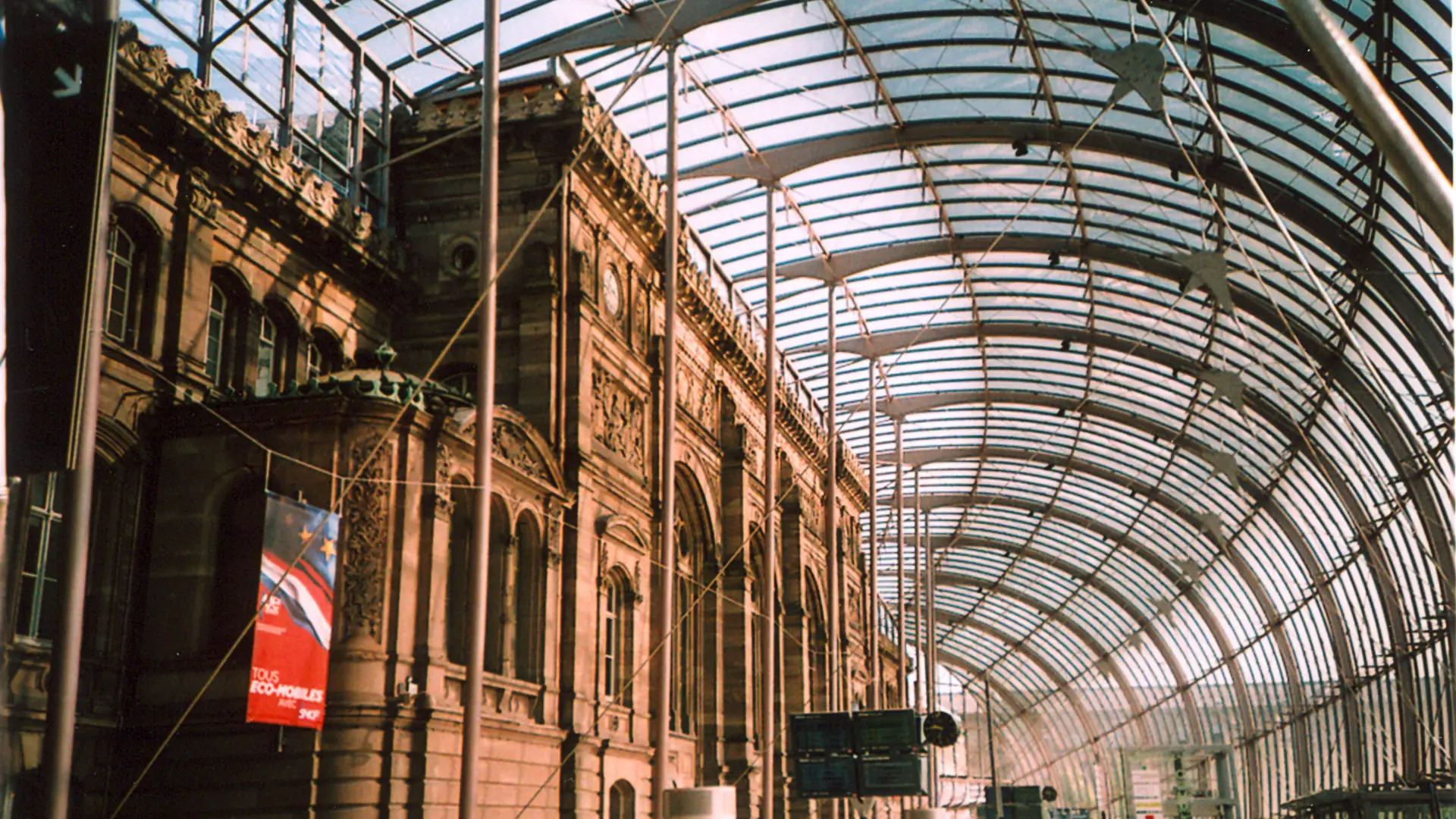 Daylight through Strasbourg station’s glass canopy beside its historic facade
