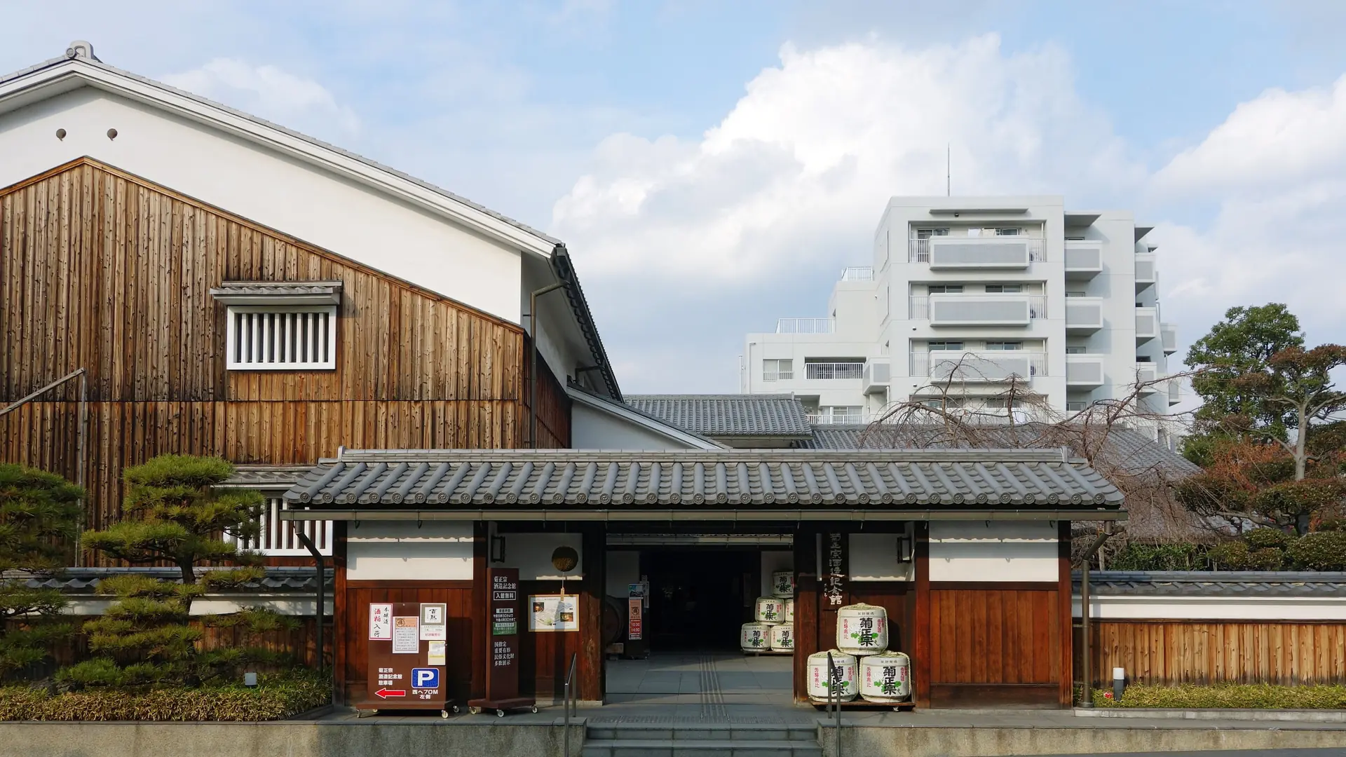 Kikumasamune Sake Brewery Museum’s wooden entrance and sake barrels under a bright blue sky in Kobe’s Higashinada district