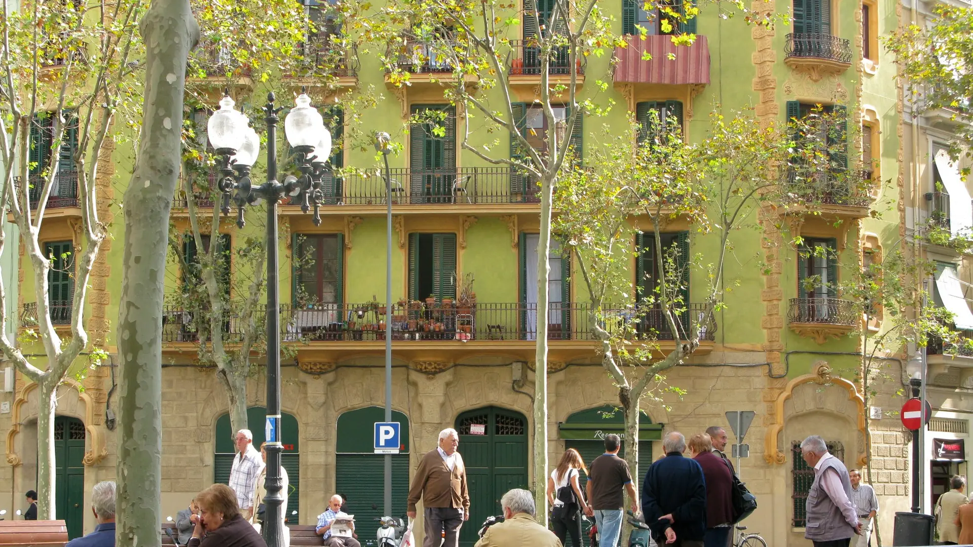 People sitting beneath trees and Modernista balconies on Rambla del Poblenou in Barcelona