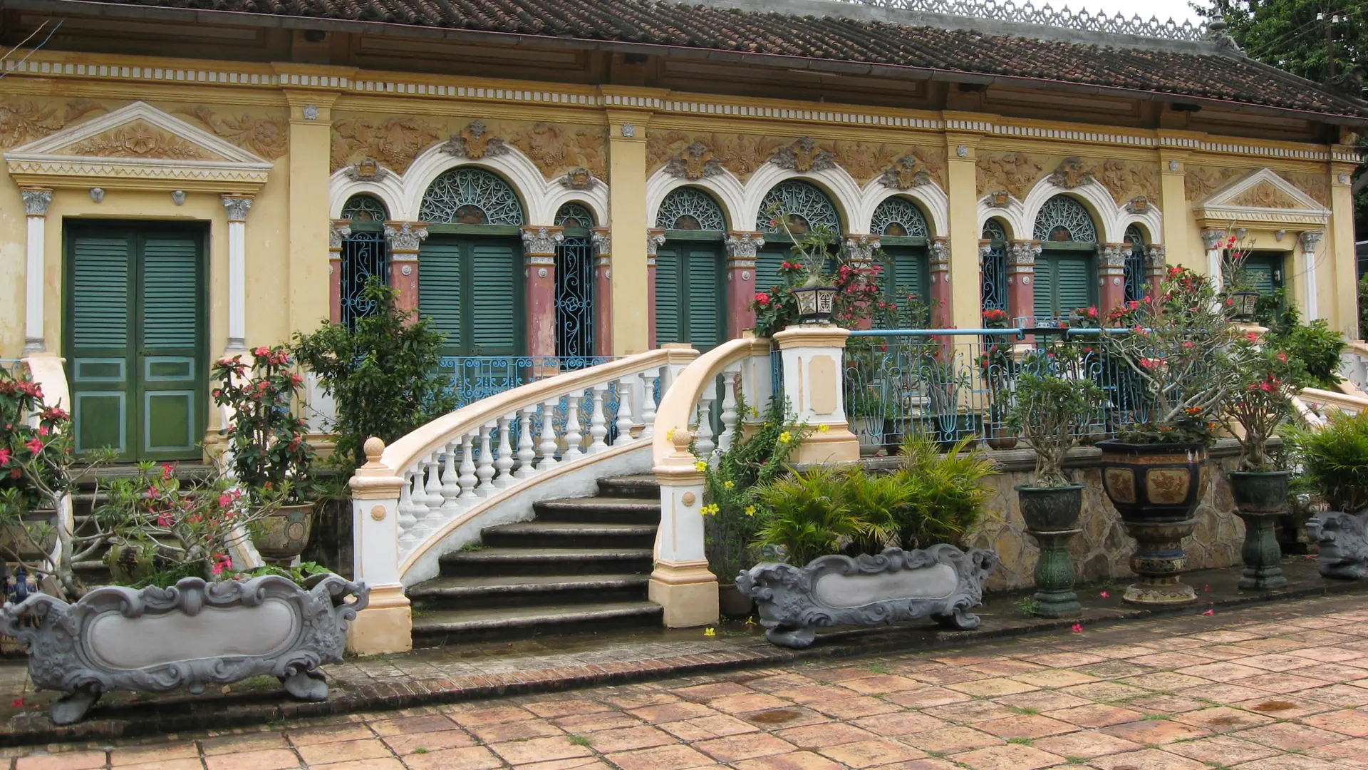 Green arched shutters, yellow facade and curved white stairs at Binh Thuy ancient house in Can Tho