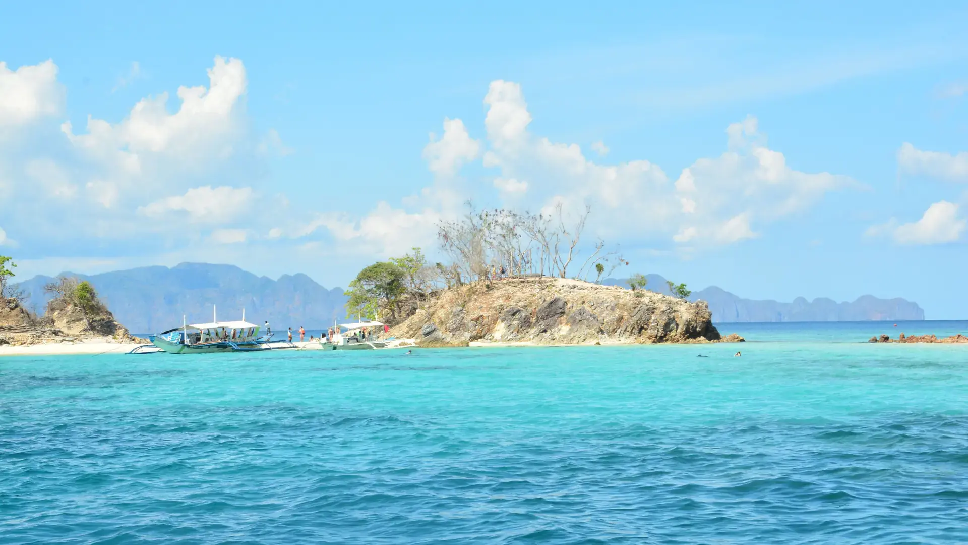 Island-hopping boats moored beside Bulog Dos island's white sand near Coron