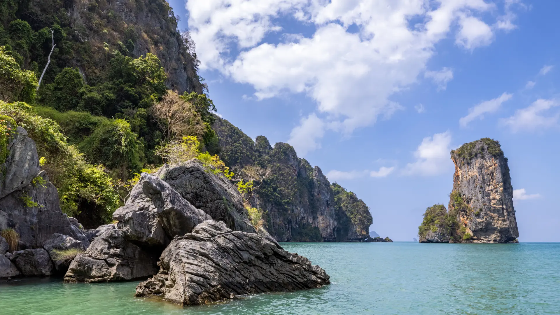 Ao Nang's clear shallows below a forested Krabi limestone cliff