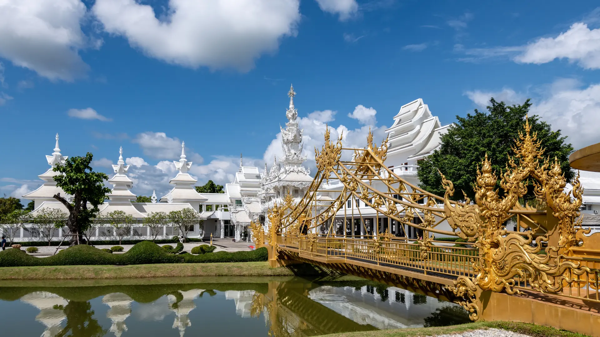 Wat Rong Khun's ornate bridge reflected in a calm Chiang Rai pond