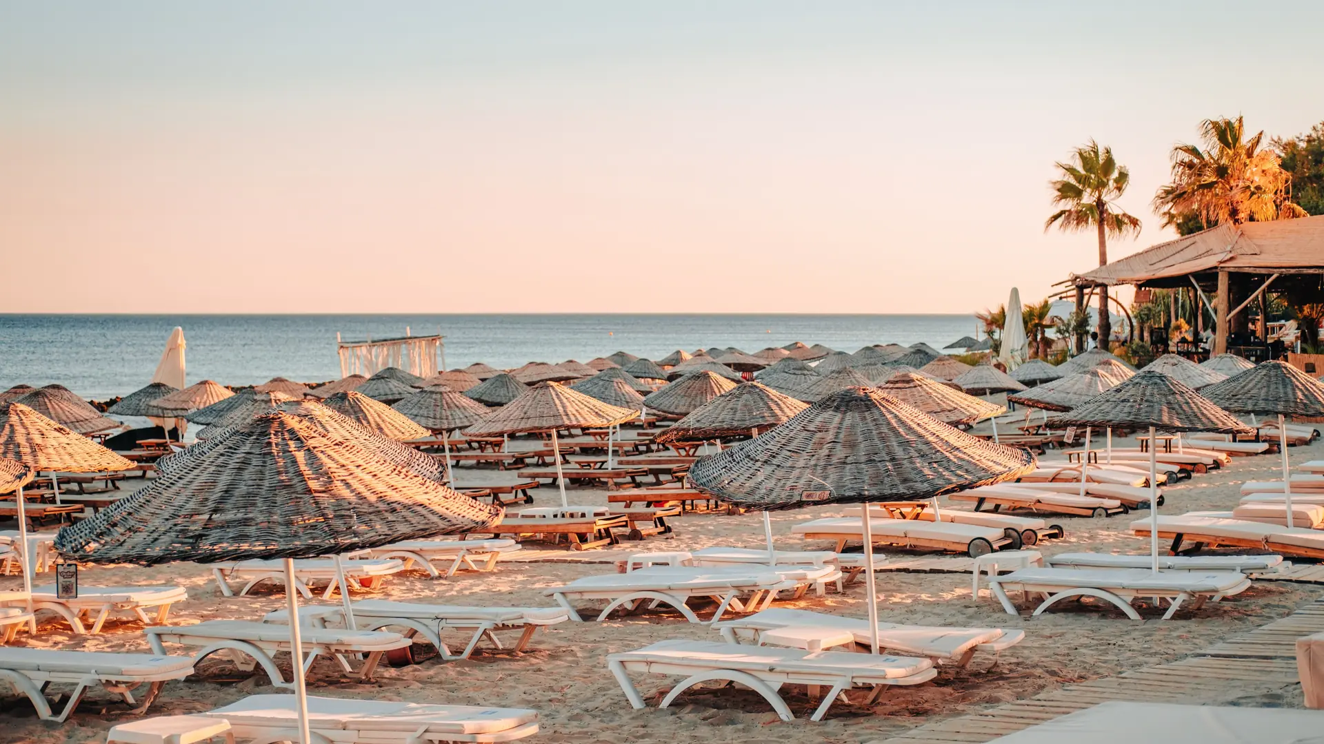 Sandy Mediterranean resort beach with straw umbrellas and empty sunbeds beneath a clear sky