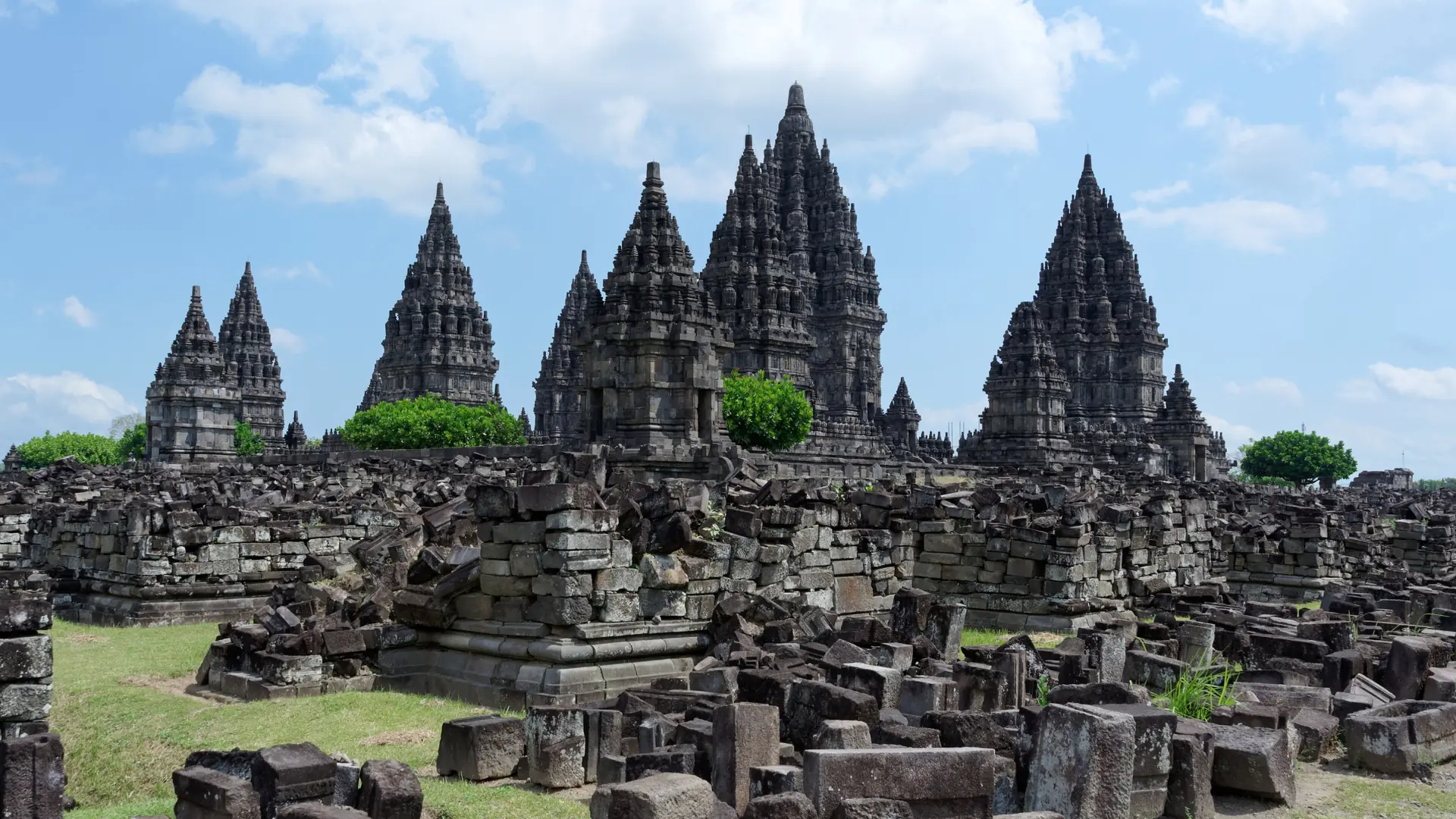Prambanan’s stone temple towers and reconstructed ruins beneath a bright blue sky