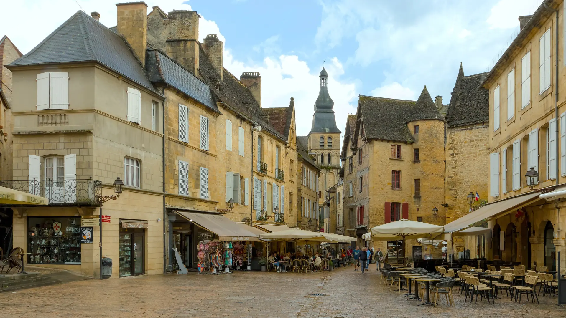 Café terraces and golden-stone façades around Place de la Liberté in Sarlat, with Saint-Sacerdos cathedral’s tower beyond