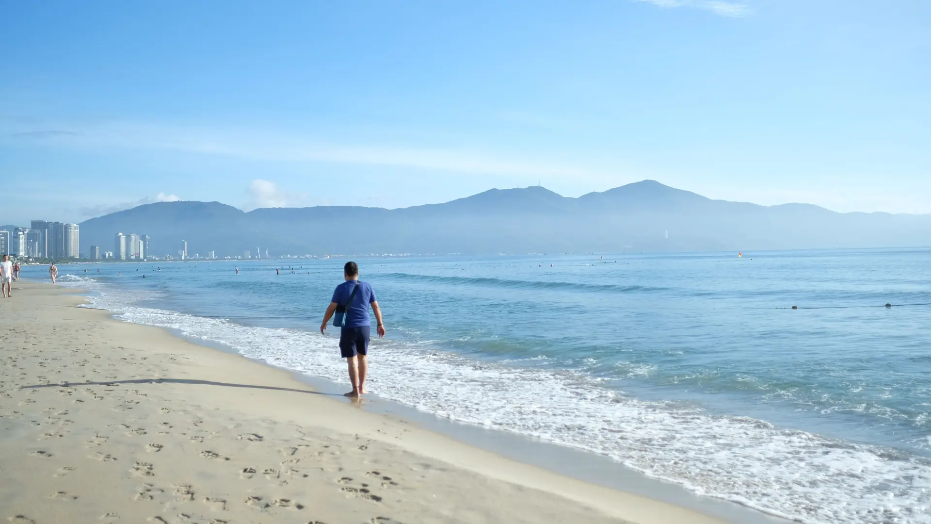 A walker on a sunny Da Nang beach beneath a blue sky