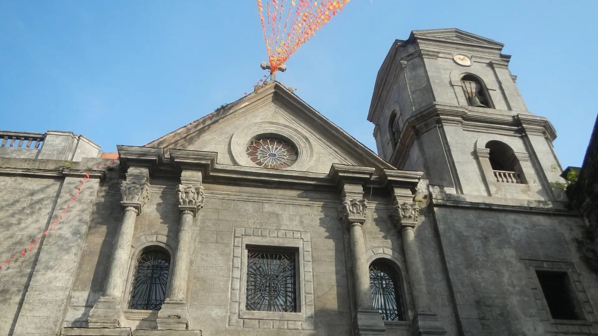 The stone facade and bell tower of San Agustin Church in Intramuros beneath a blue sky