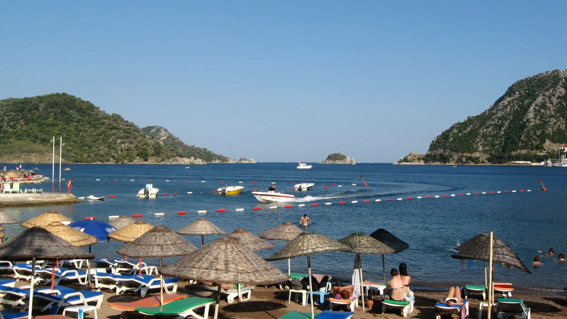 Bright İçmeler bay, rocky headlands and beach parasols, shown as a wider Marmaris district scene