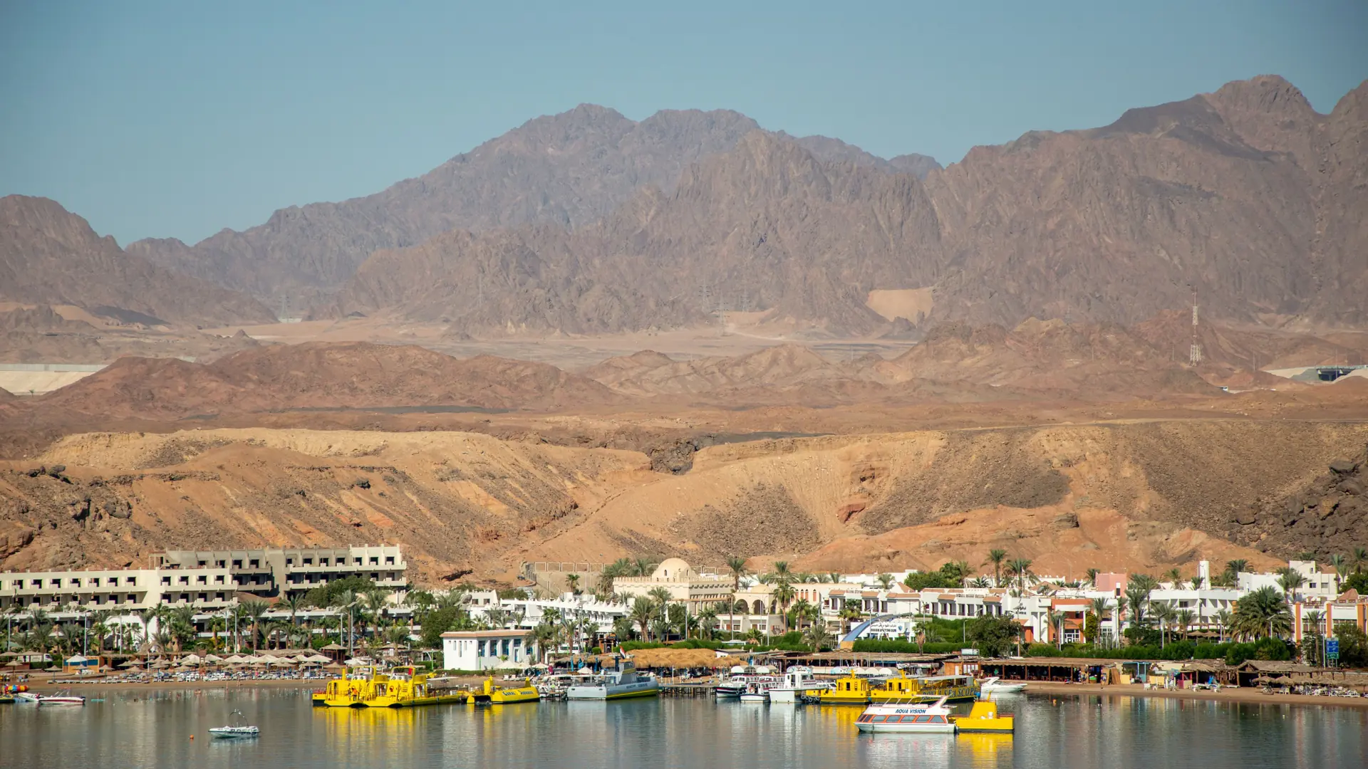 Sunny Red Sea resort shore with desert mountains behind the water