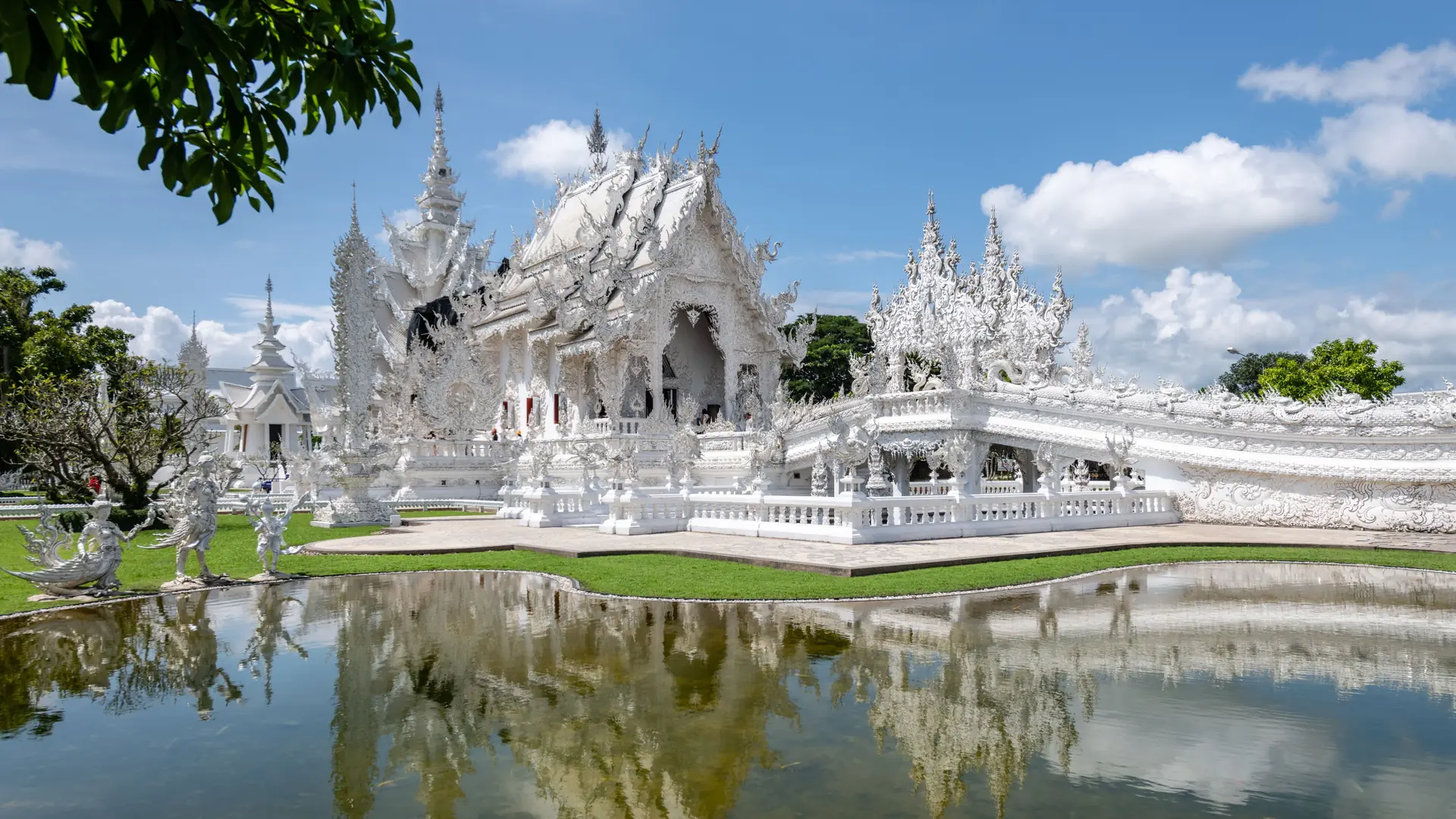 Wat Rong Khun's white ornament and mirrored pond under a blue sky