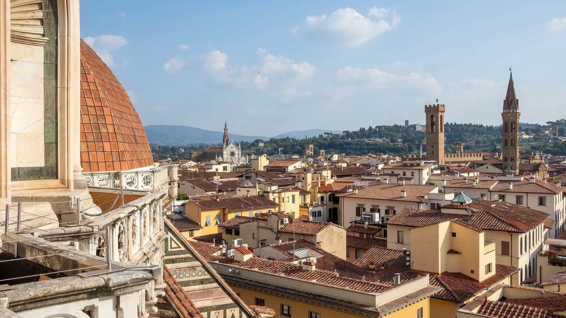 Florence Cathedral’s dome and bell tower rising over the city’s terracotta rooftops under a bright blue sky.