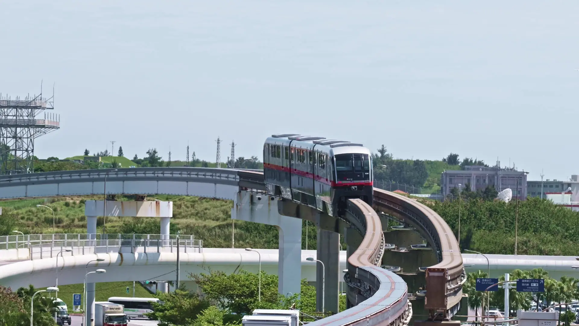 Yui Rail trains leaving Naha Airport Station above green airport-side landscape