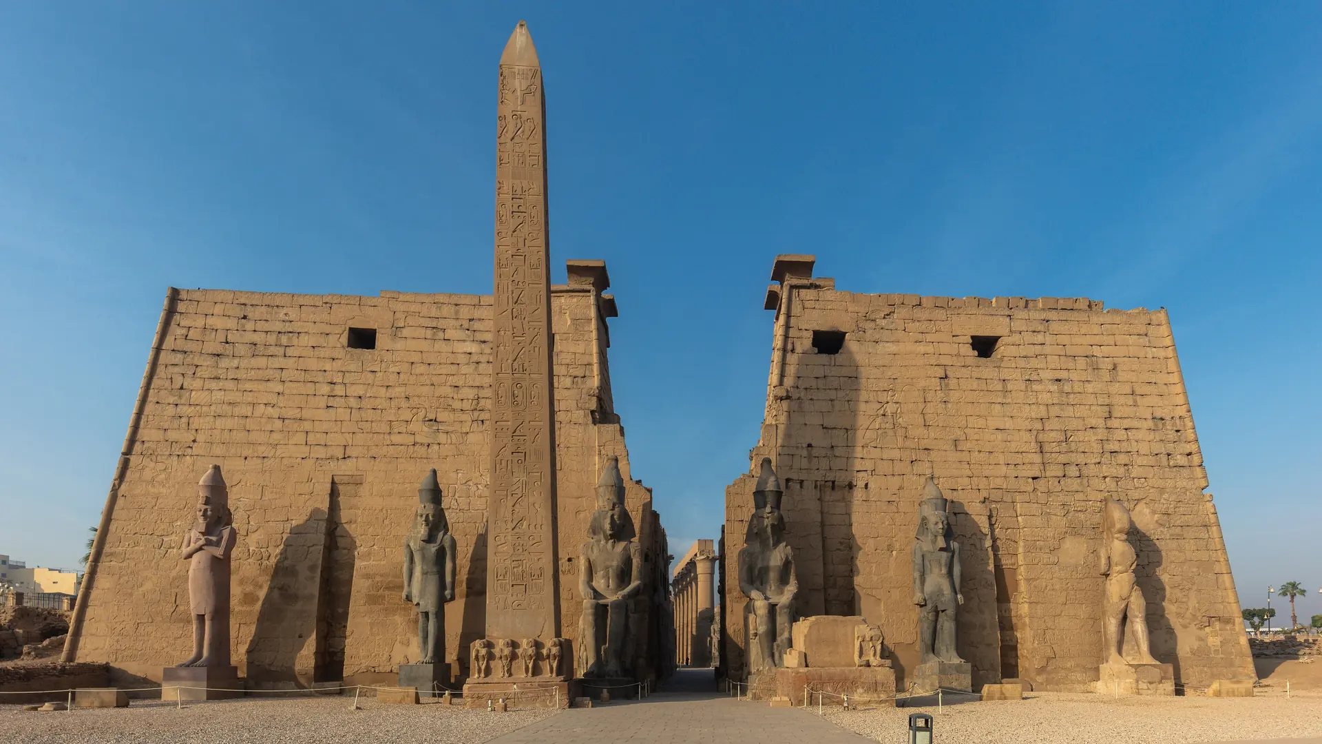 Luxor Temple’s stone pylon, seated statues and obelisk under a clear blue sky