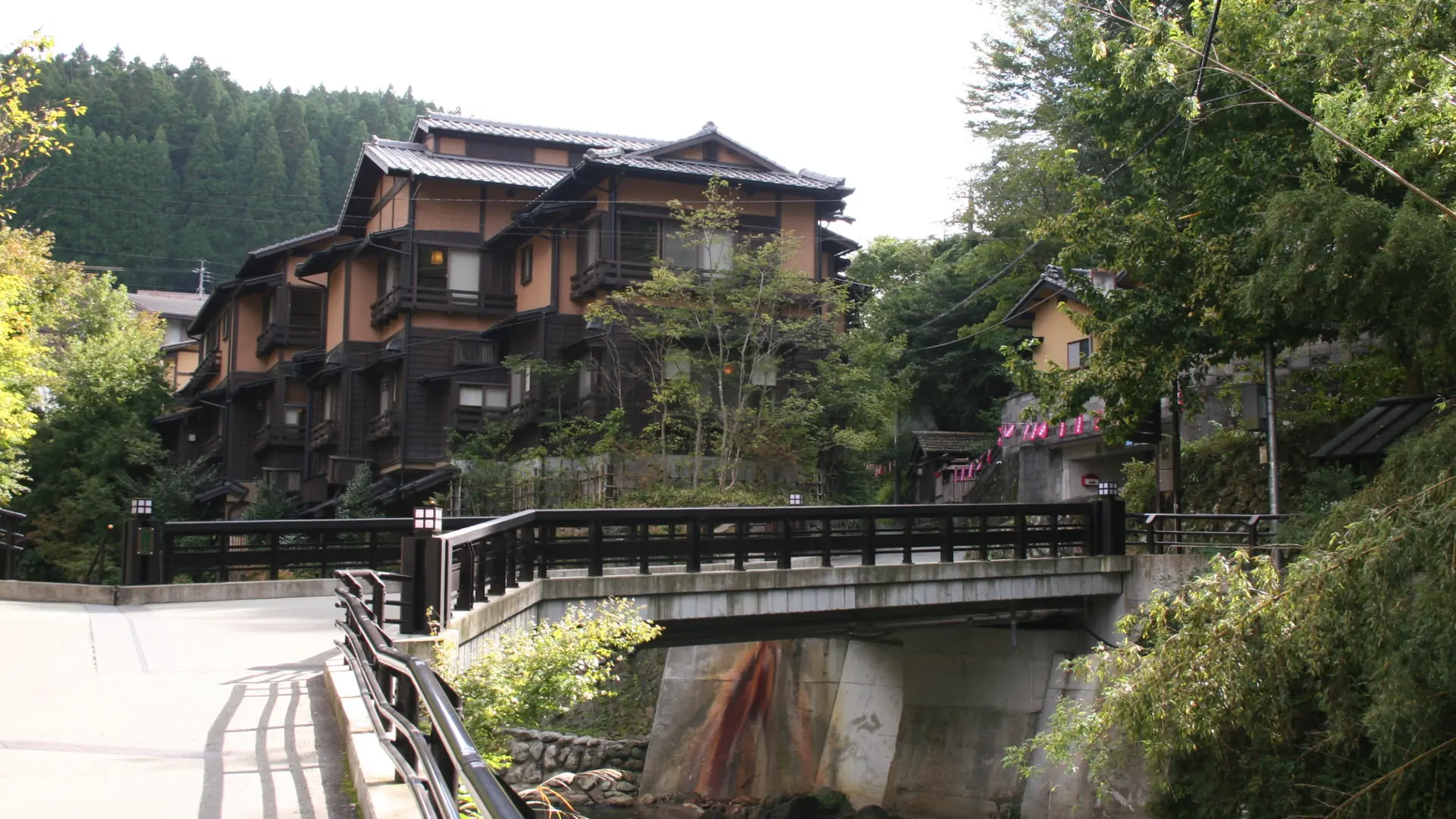 Sunlit wooden buildings and a small bridge beside the river in Kurokawa Onsen.