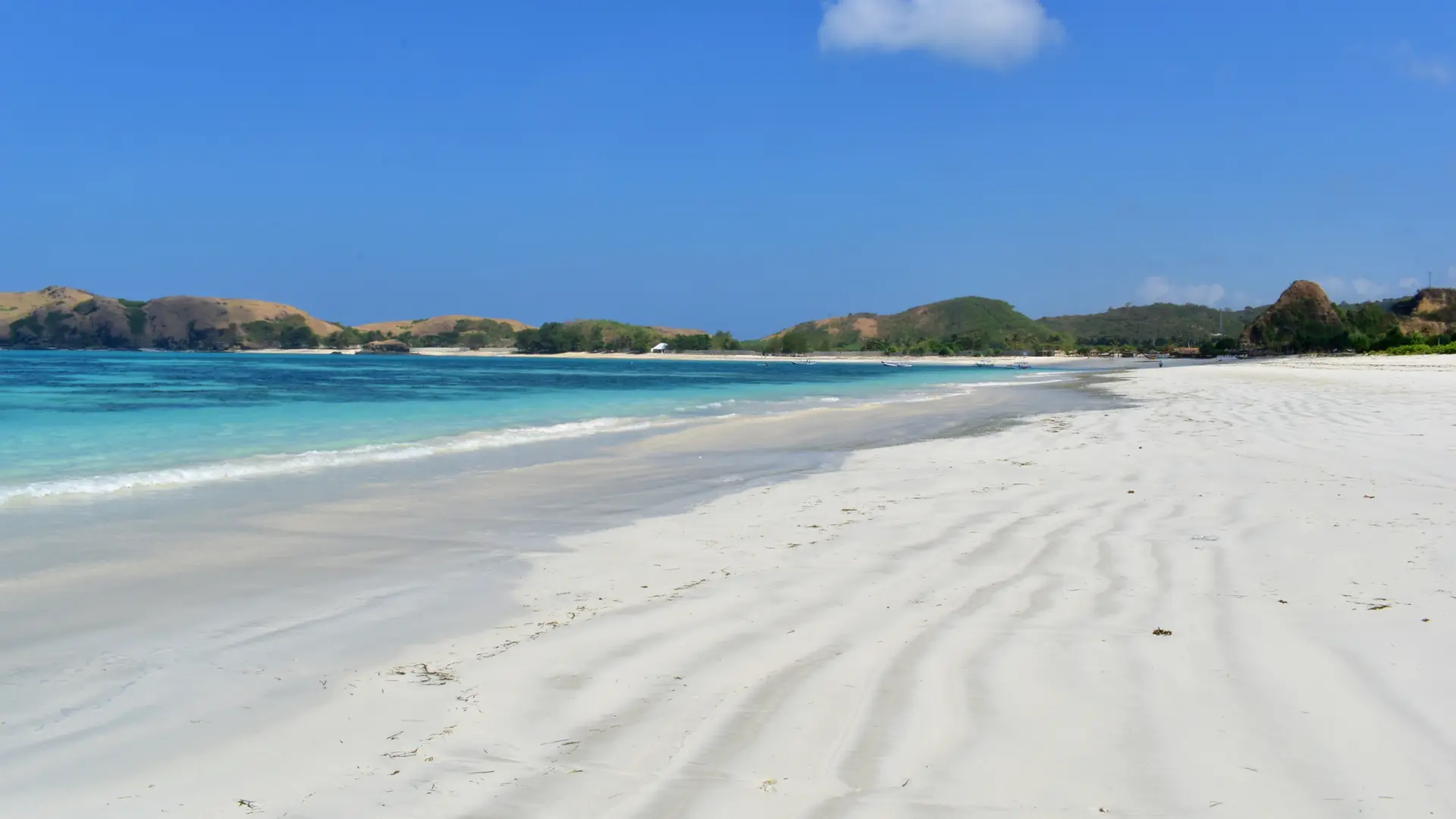 White sand and turquoise shallows at Tanjung Aan on southern Lombok beneath a bright blue sky