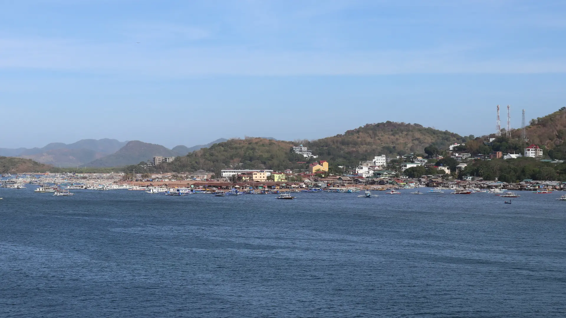Coron town’s sunlit shoreline and outrigger boats across the blue bay