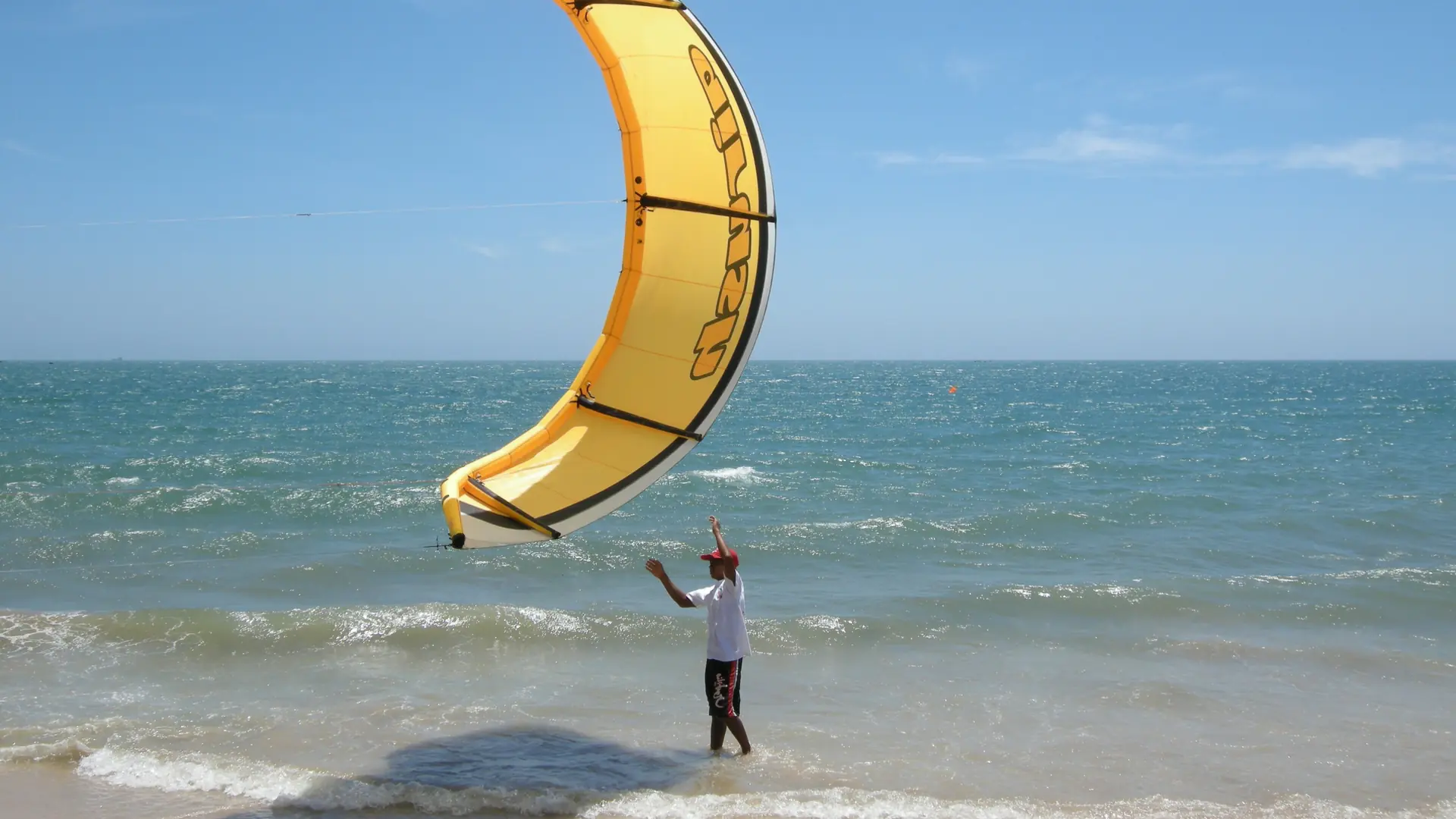 A yellow kitesurfing kite held above Mui Ne beach, a wider coastal scene